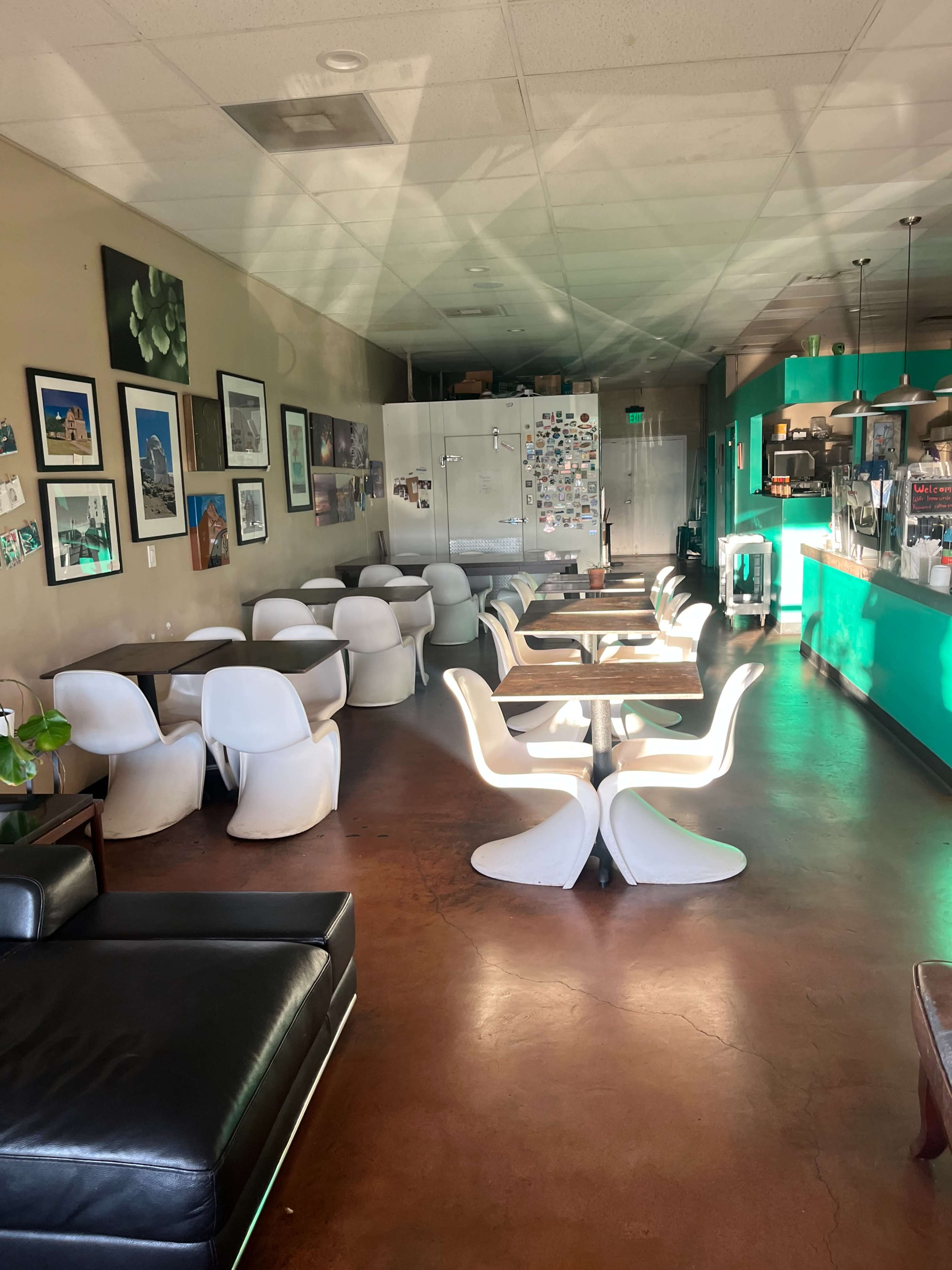 A spacious cafe with white chairs and tables, green accent walls, and various artwork displayed on the walls.