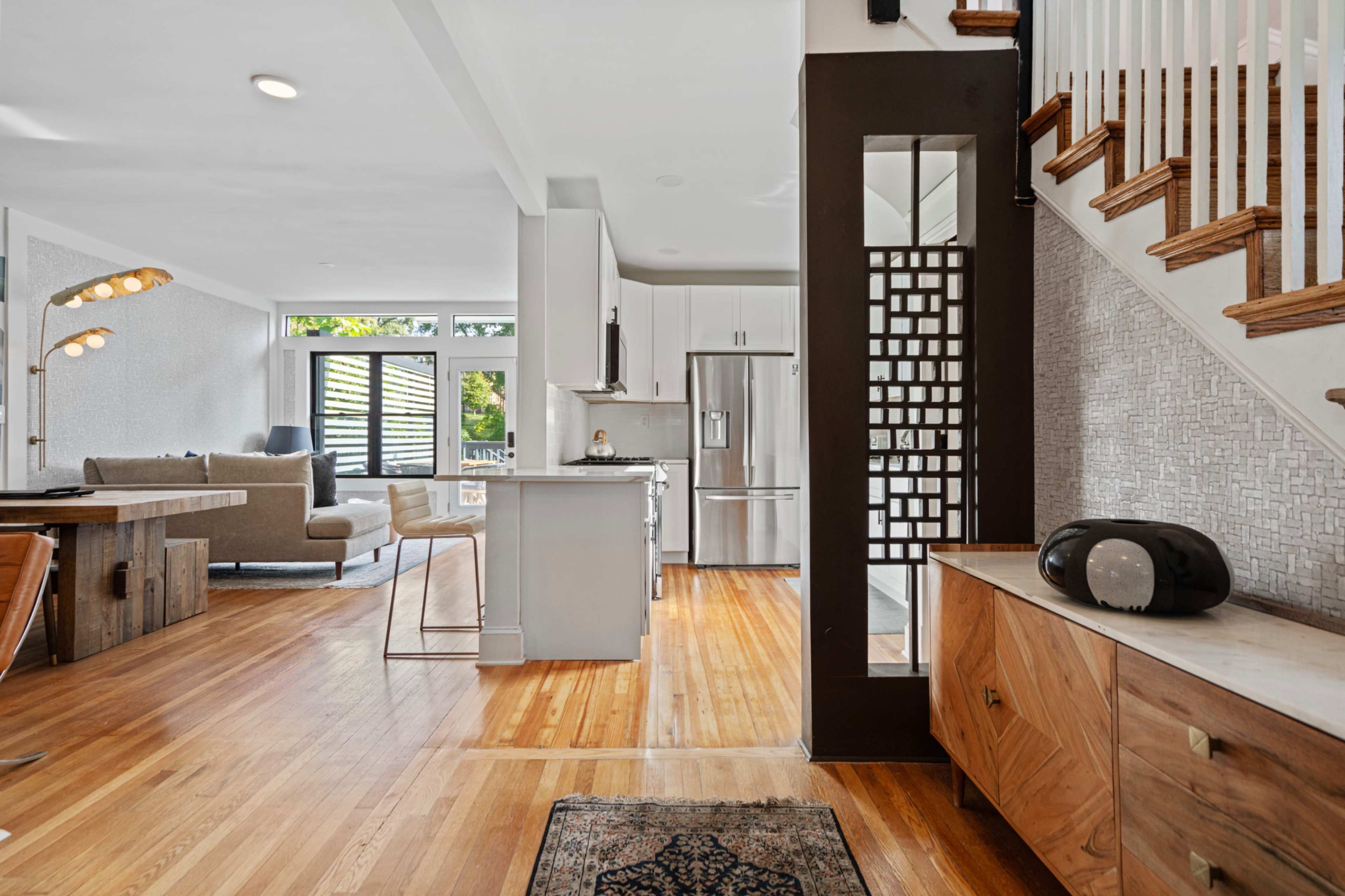 A modern interior featuring a kitchen with stainless steel appliances, a living area with a sofa, and a staircase leading to an upper level.
