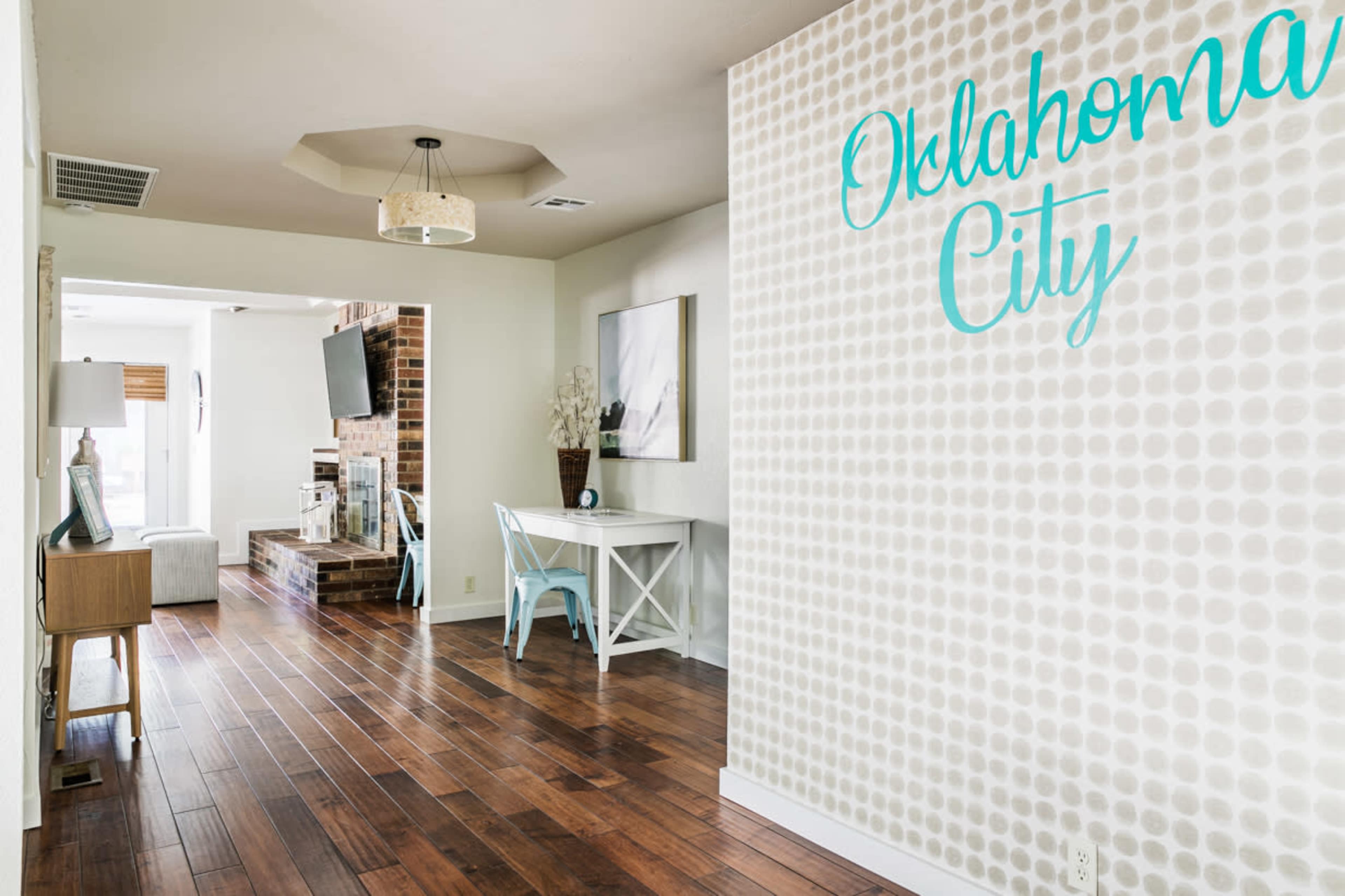 A modern entryway with a statement wall that reads "Oklahoma City," leading to a living area with wooden flooring and a simple work desk.