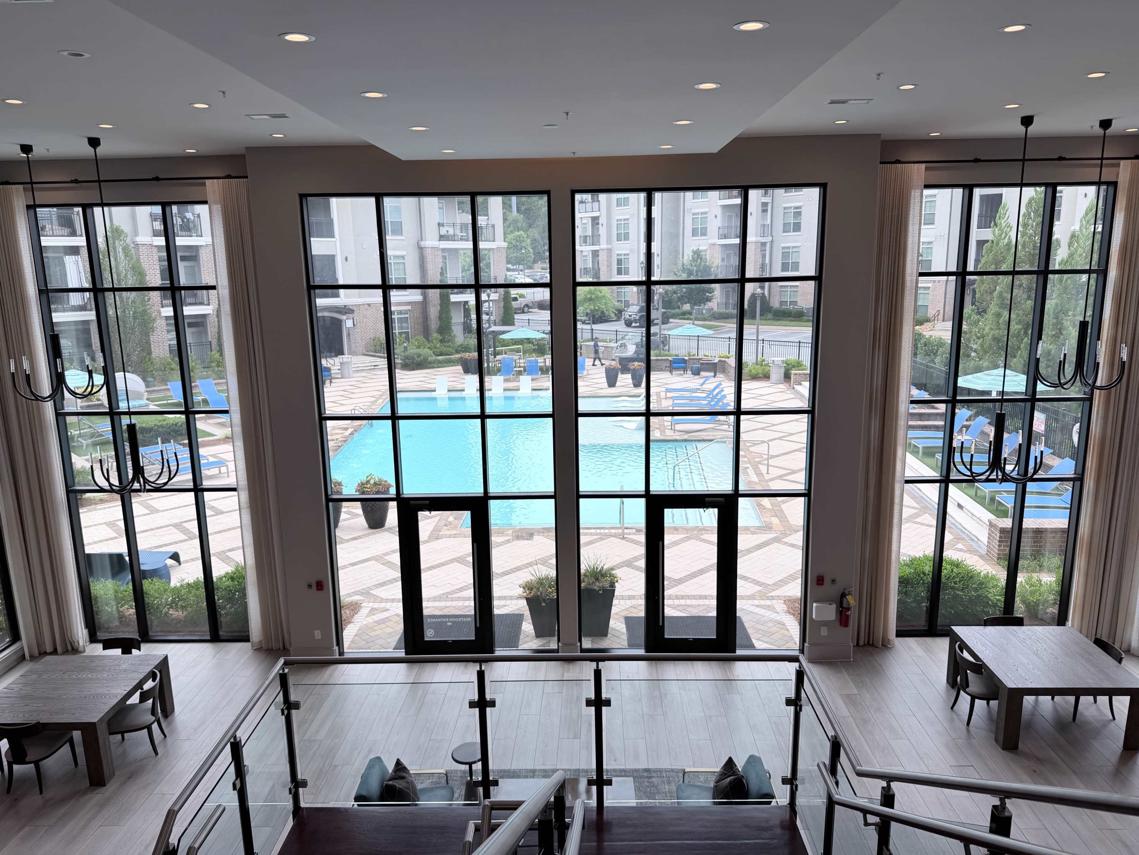 The image shows a large window overlooking a swimming pool area with lounge chairs and umbrellas, framed by elegant interior design elements.