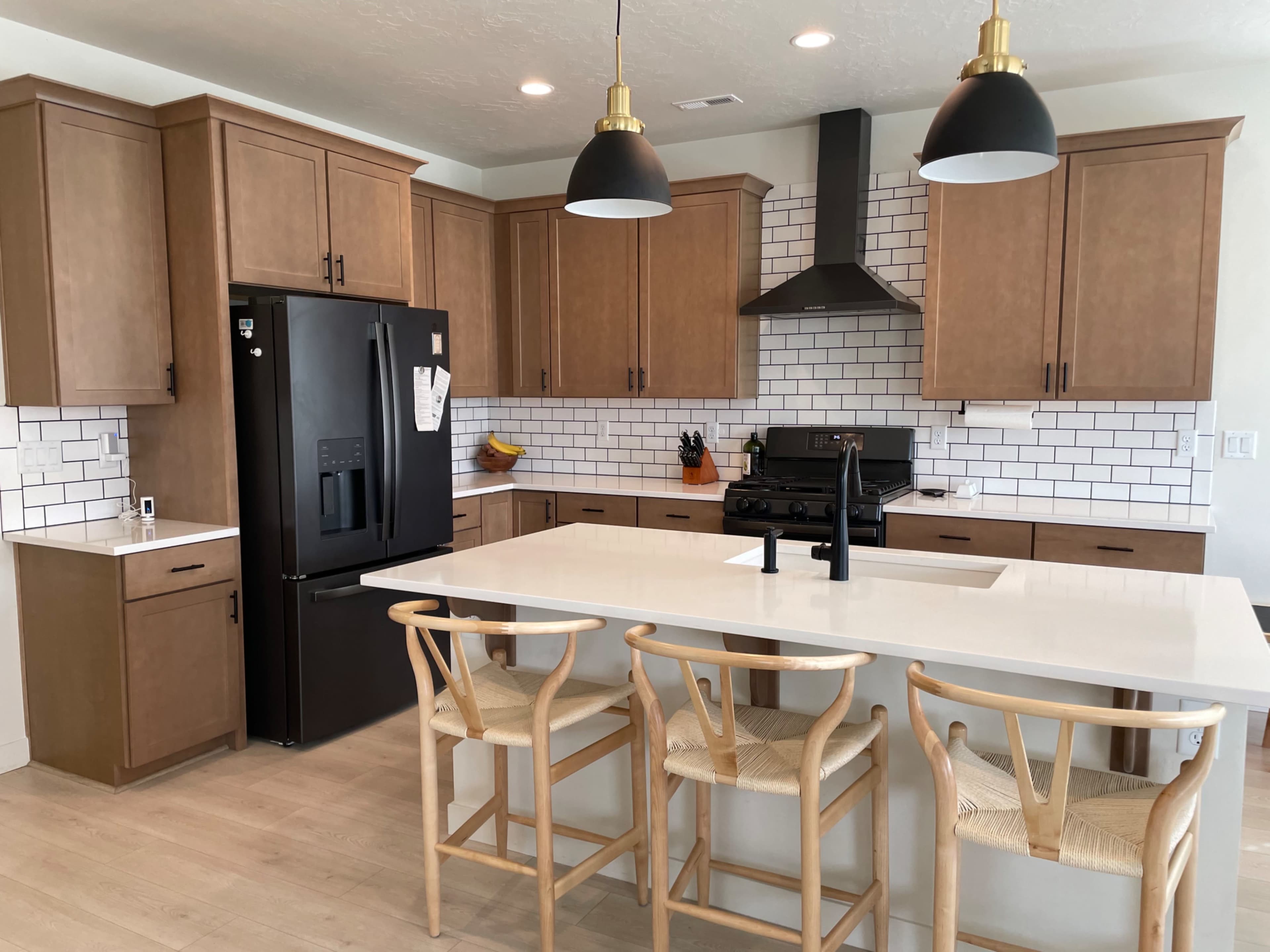 A modern kitchen with wooden cabinetry, a black refrigerator, a gas stove, and an island with bar stools.