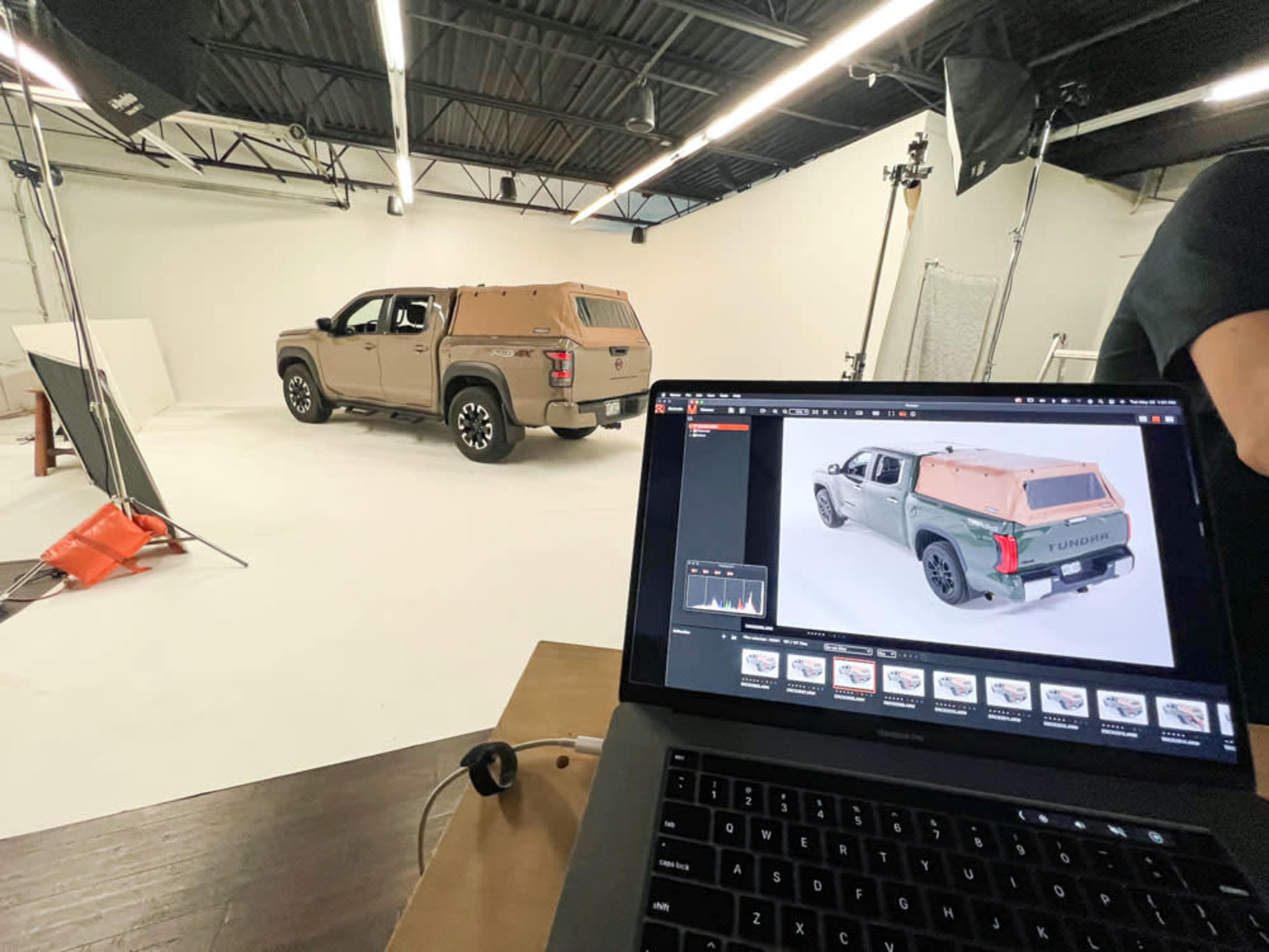 A vehicle is parked in a photography studio with a laptop displaying images of the same vehicle.