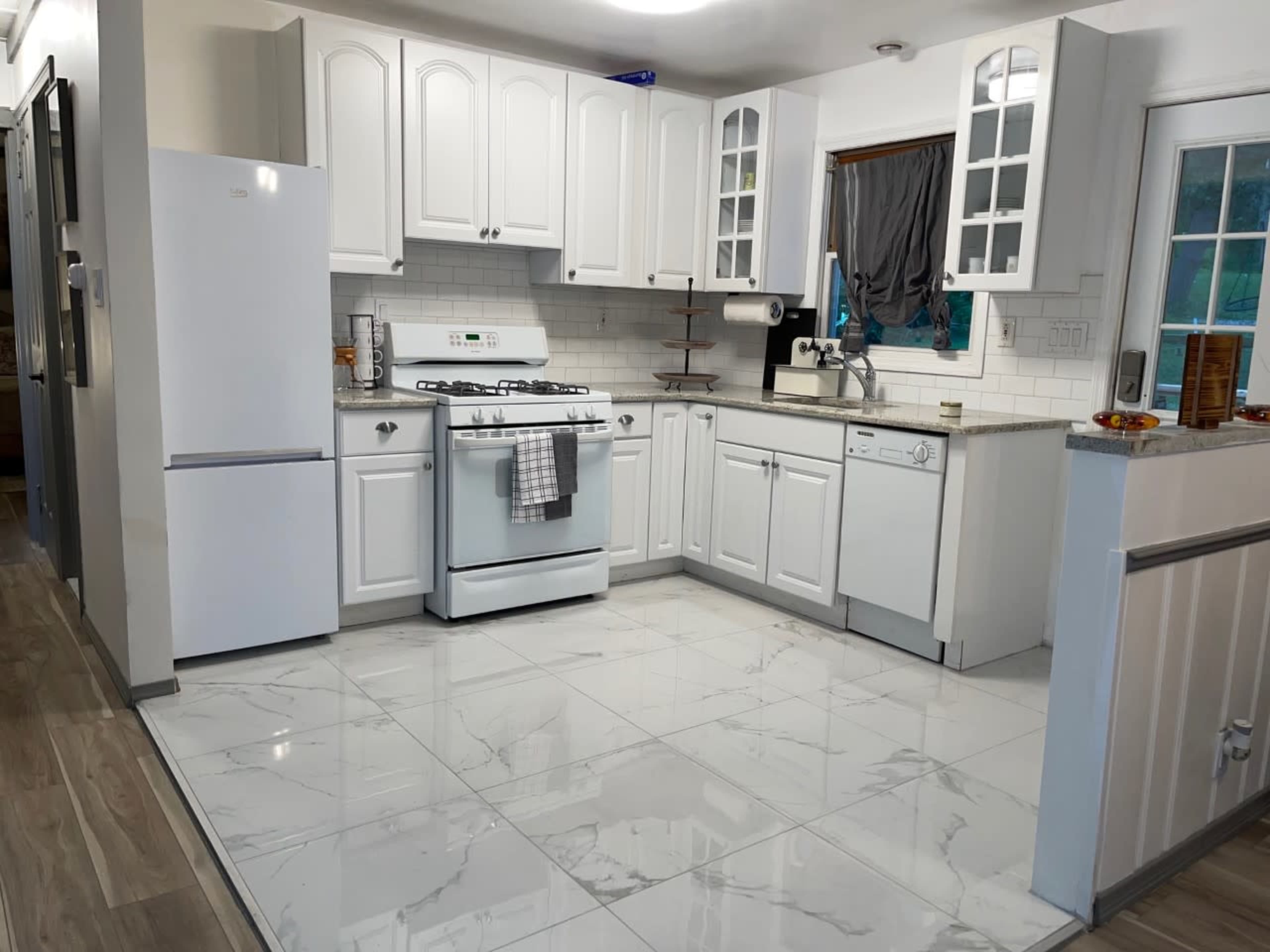 A modern kitchen with white cabinetry, a gas stove, a refrigerator, and a marble-patterned tile floor.