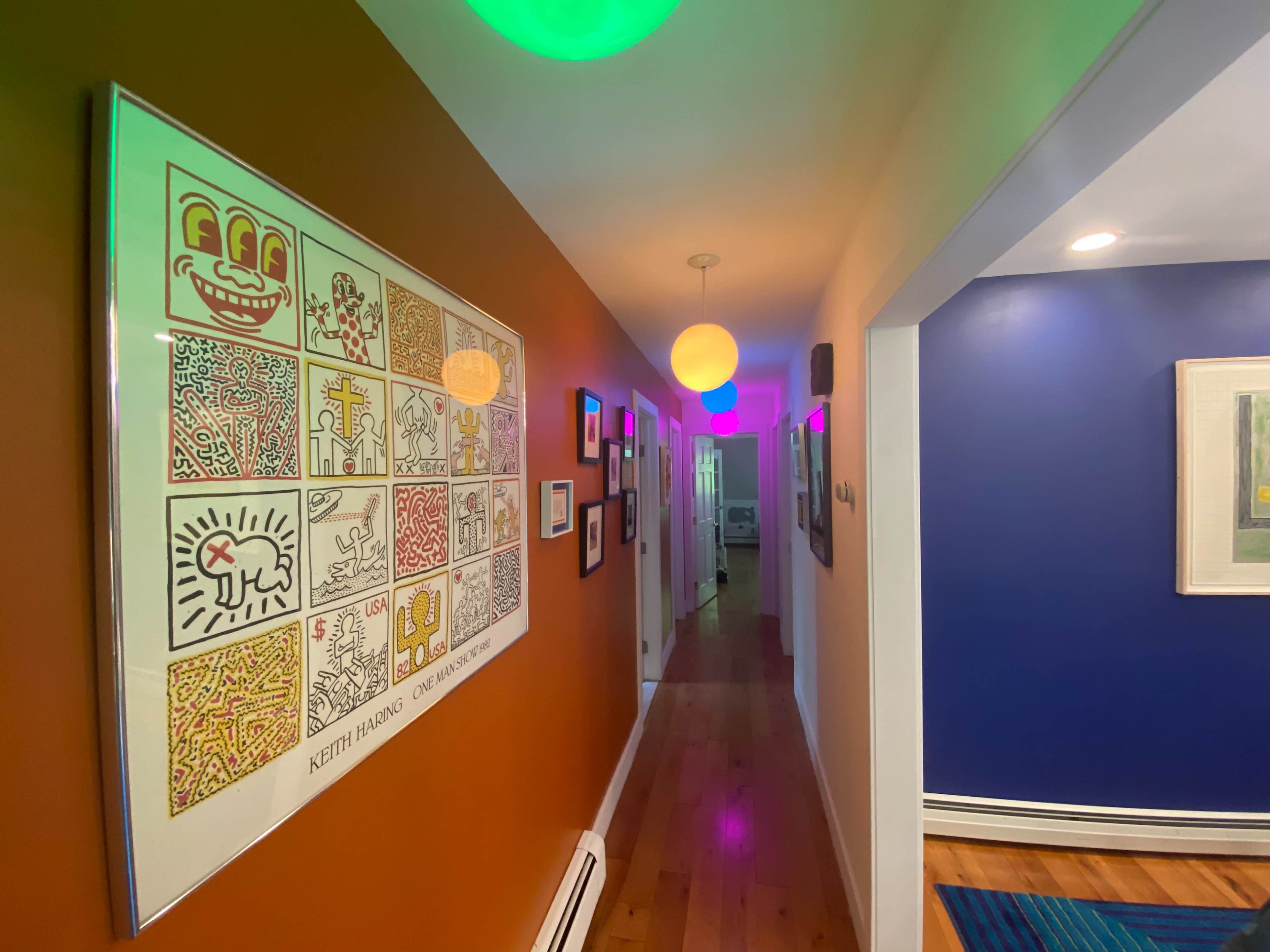 A hallway features a colorful mural by Keith Haring on one wall, with illuminated round lights and vibrant paint on the other walls.