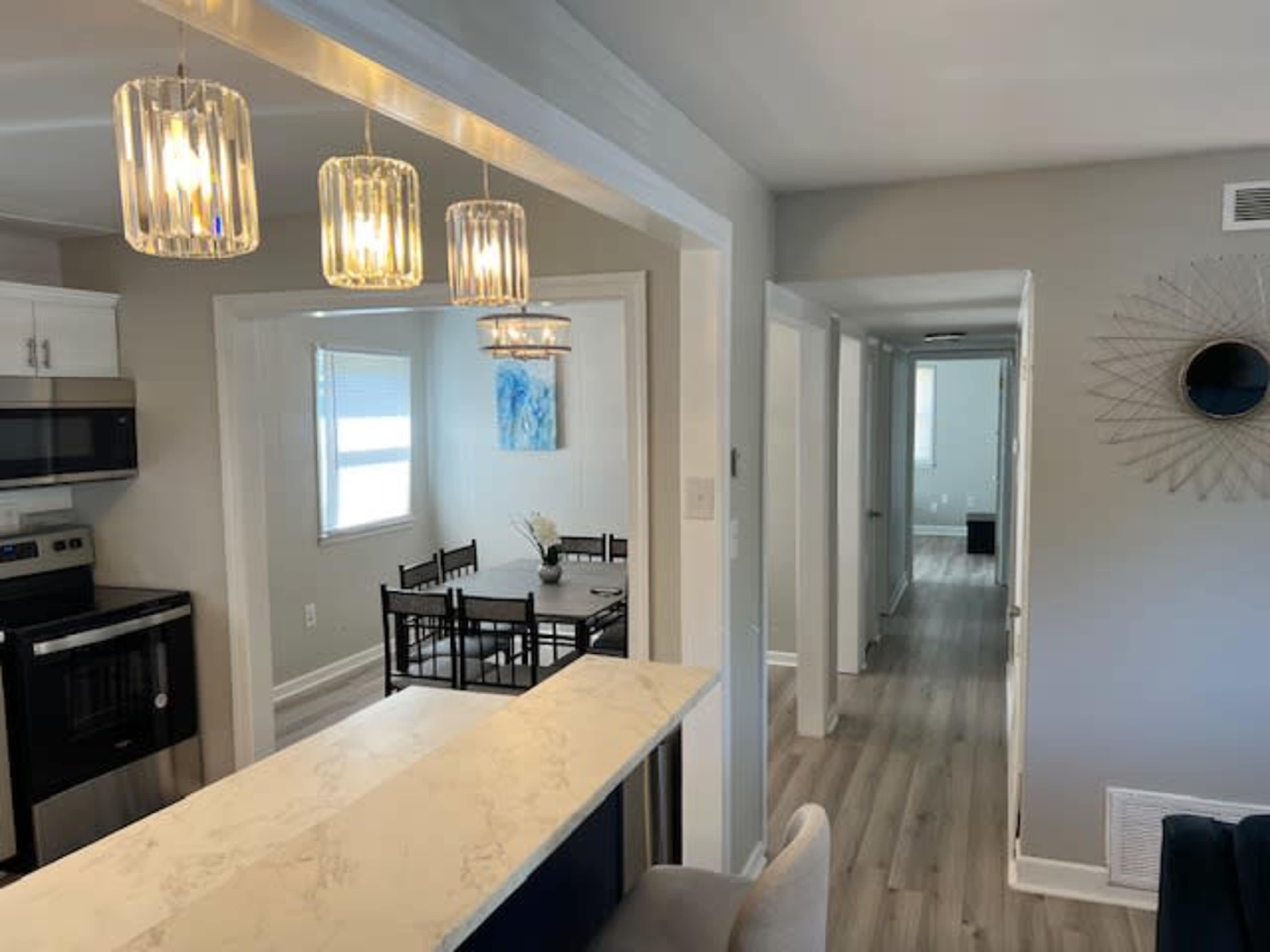 A modern, open-concept living space with a kitchen area featuring pendant lighting, a dining table in the adjacent room, and a hallway leading to more rooms.