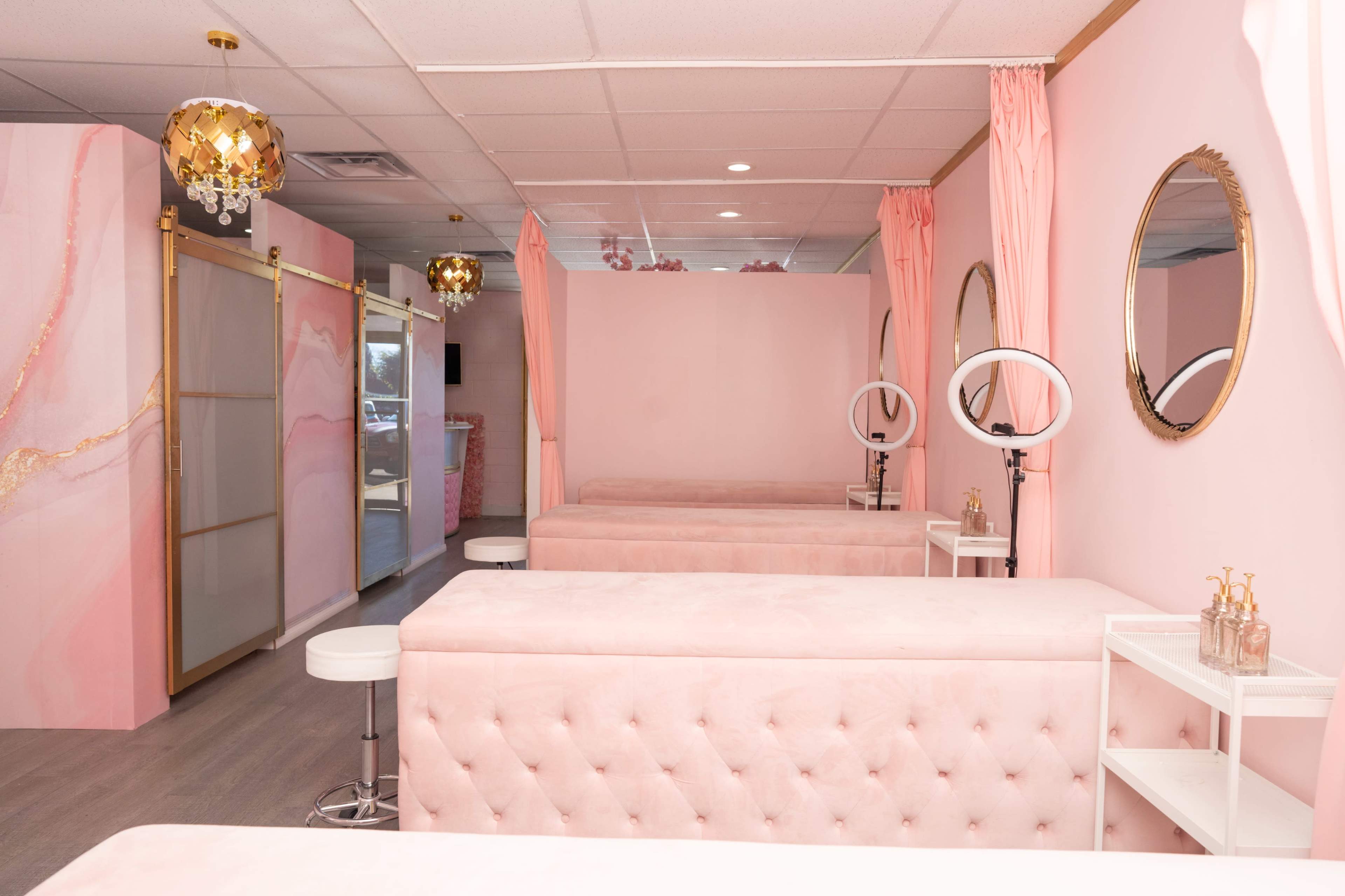 A beauty treatment room with pink walls, tufted pink treatment tables, and circular mirrors.