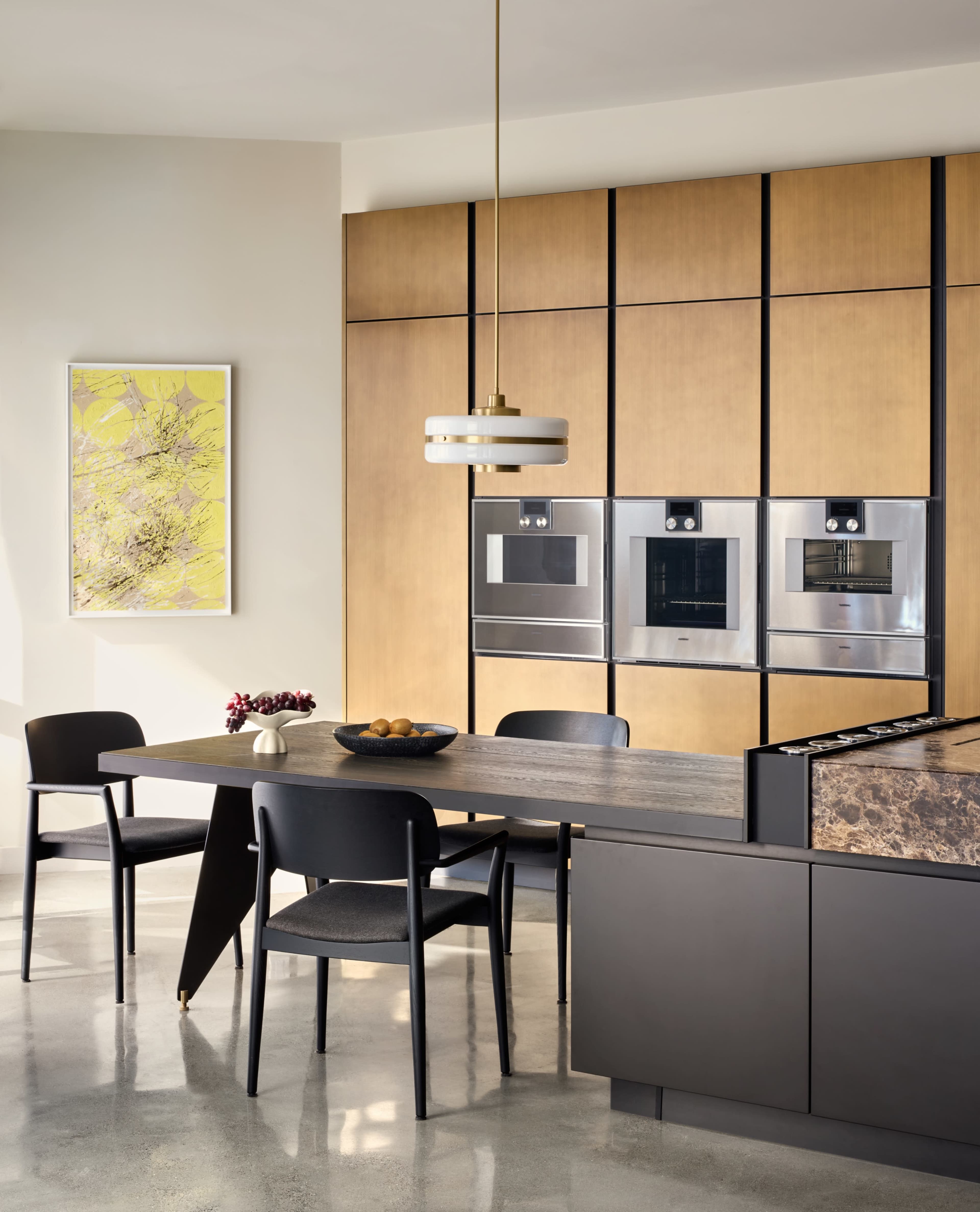The modern kitchen features a sleek design with wooden cabinetry, stainless steel appliances, and a central dining table surrounded by four black chairs.