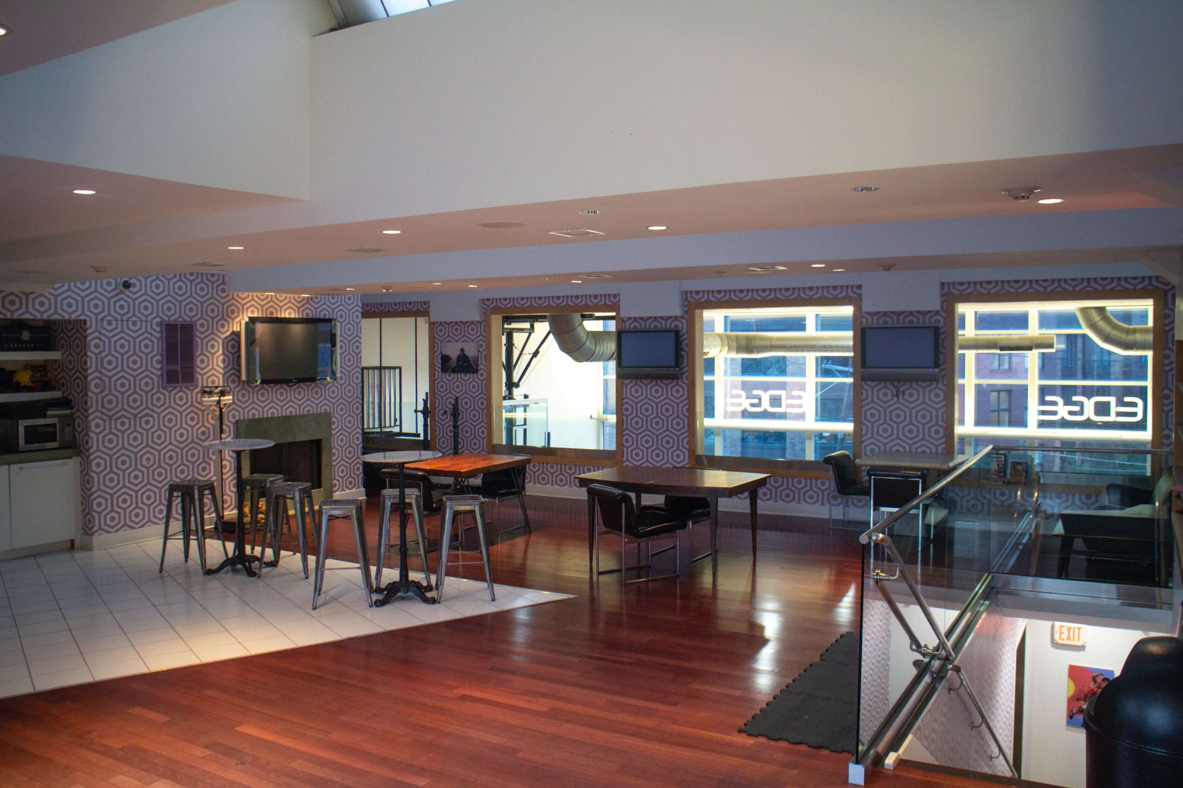 A modern interior space with hardwood flooring, seating areas, and patterned wallpaper, featuring a kitchen and multiple screens.