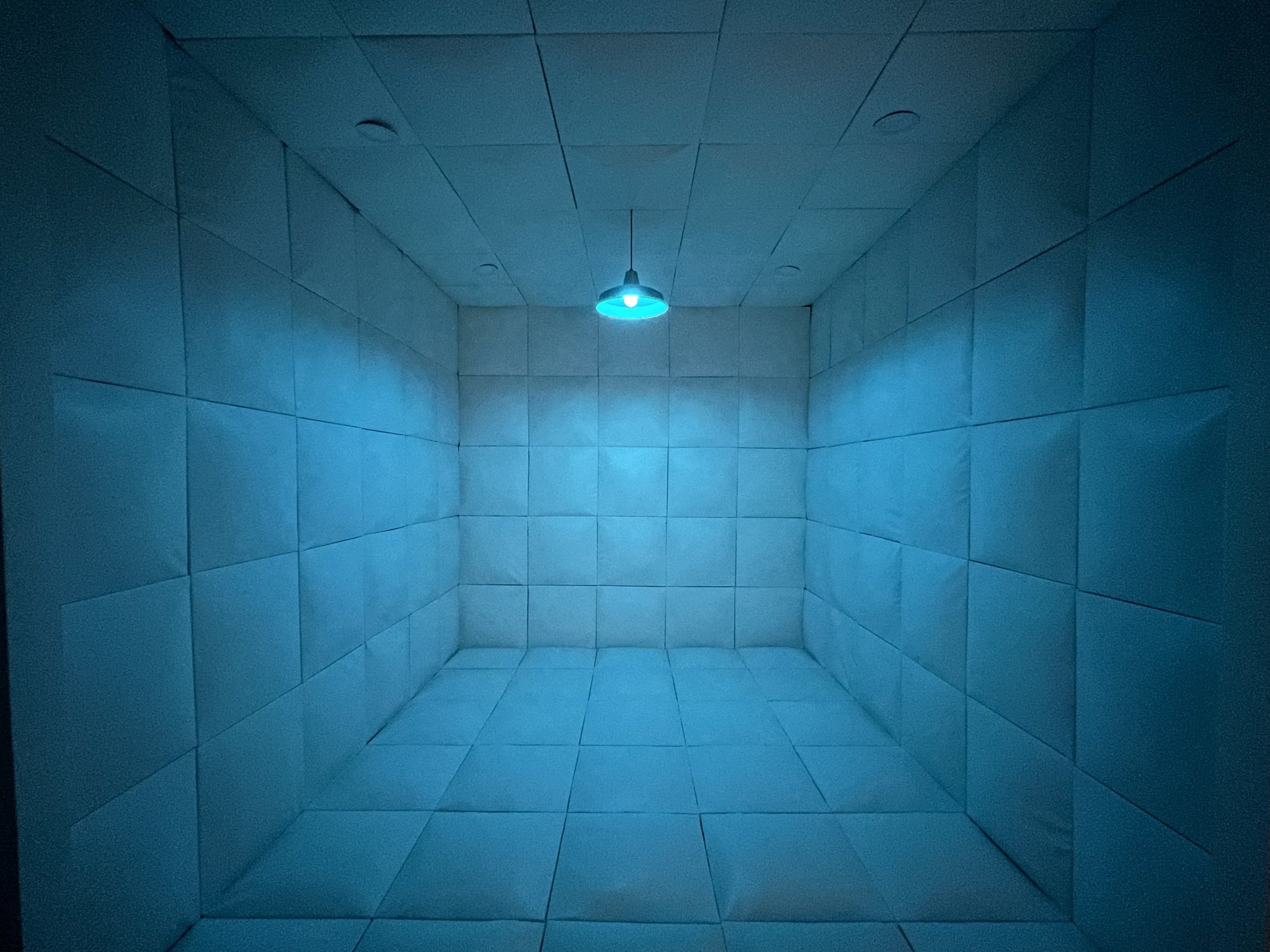 A padded room with blue lighting, featuring padded walls and a ceiling-mounted light in the center.