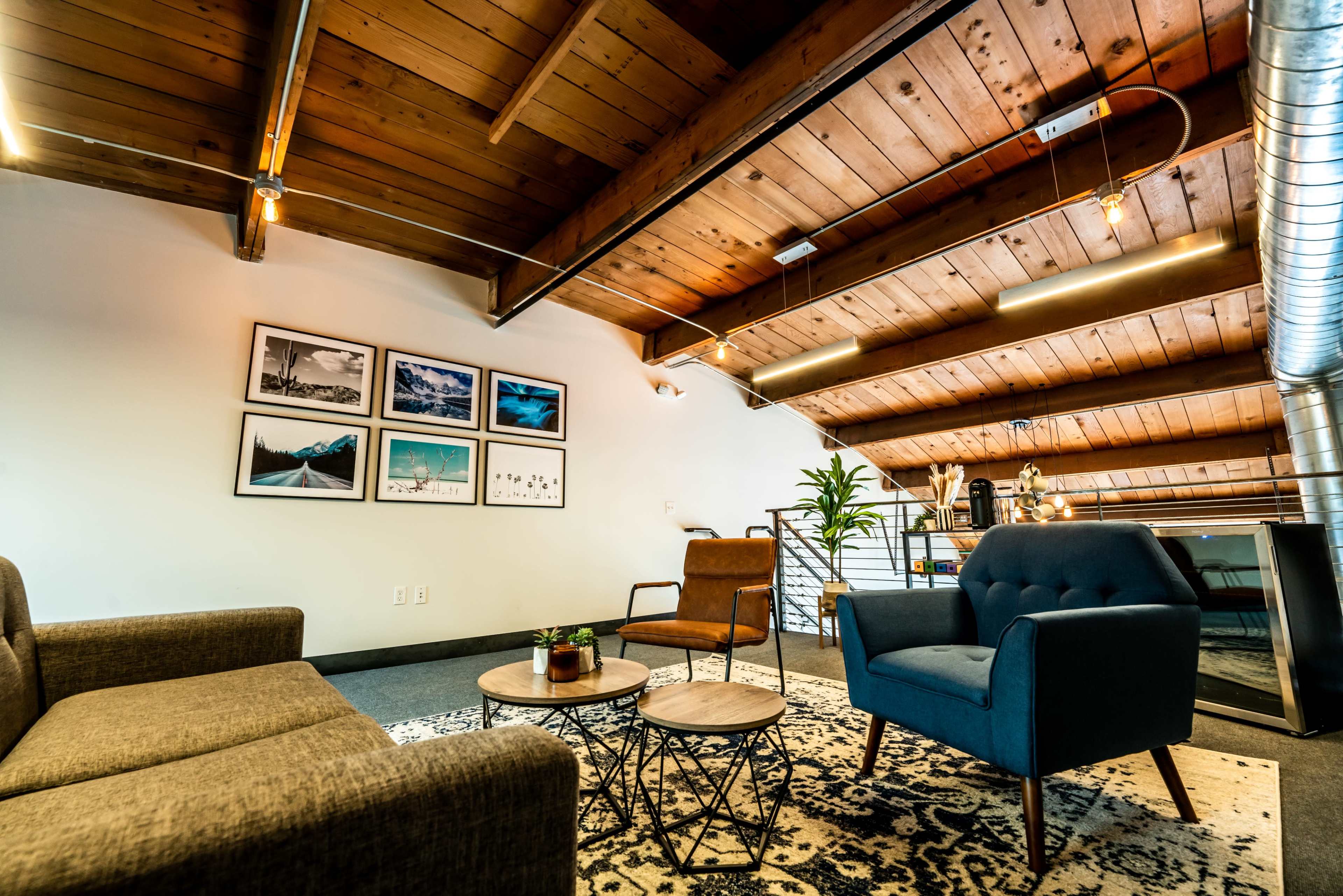 A modern lounge area with two sofas, a patterned rug, wooden beams on the ceiling, and framed pictures on the wall.