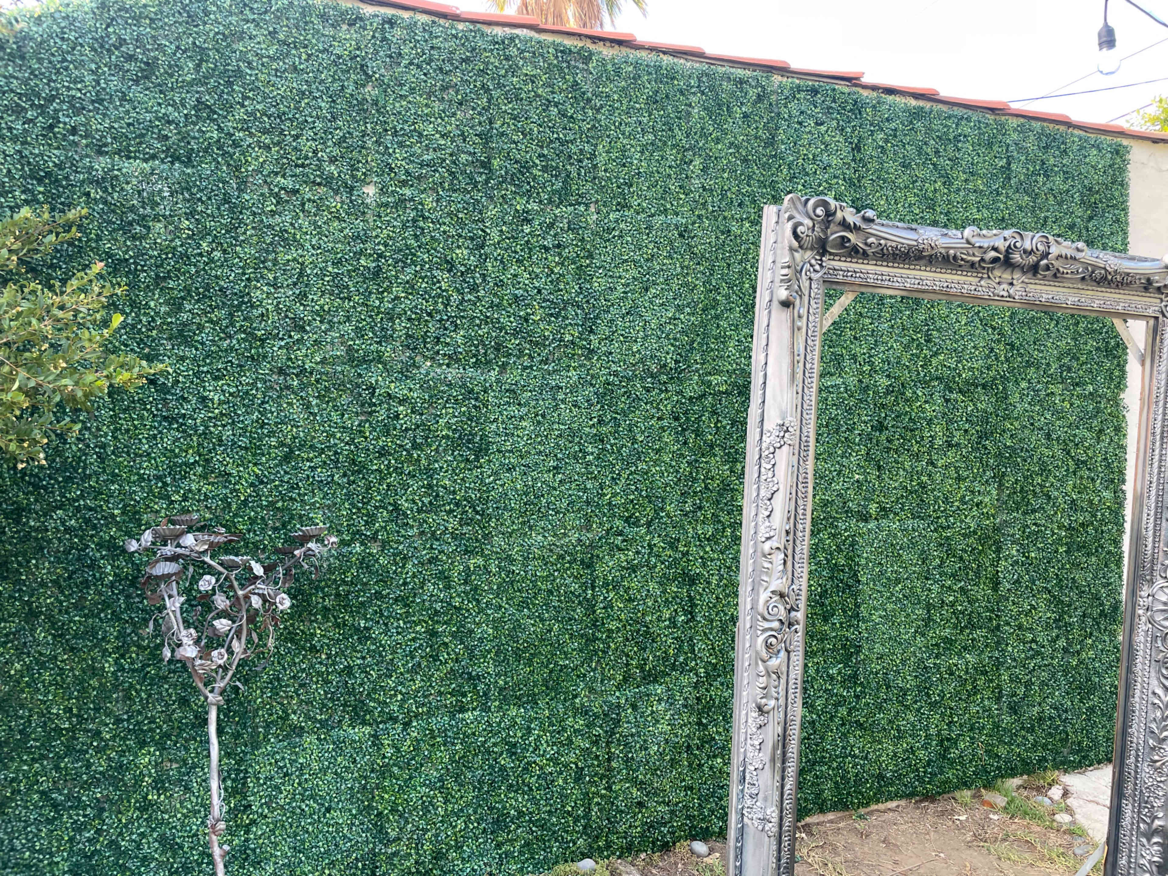 A decorative green wall of artificial foliage is paired with an ornate frame standing beside it.