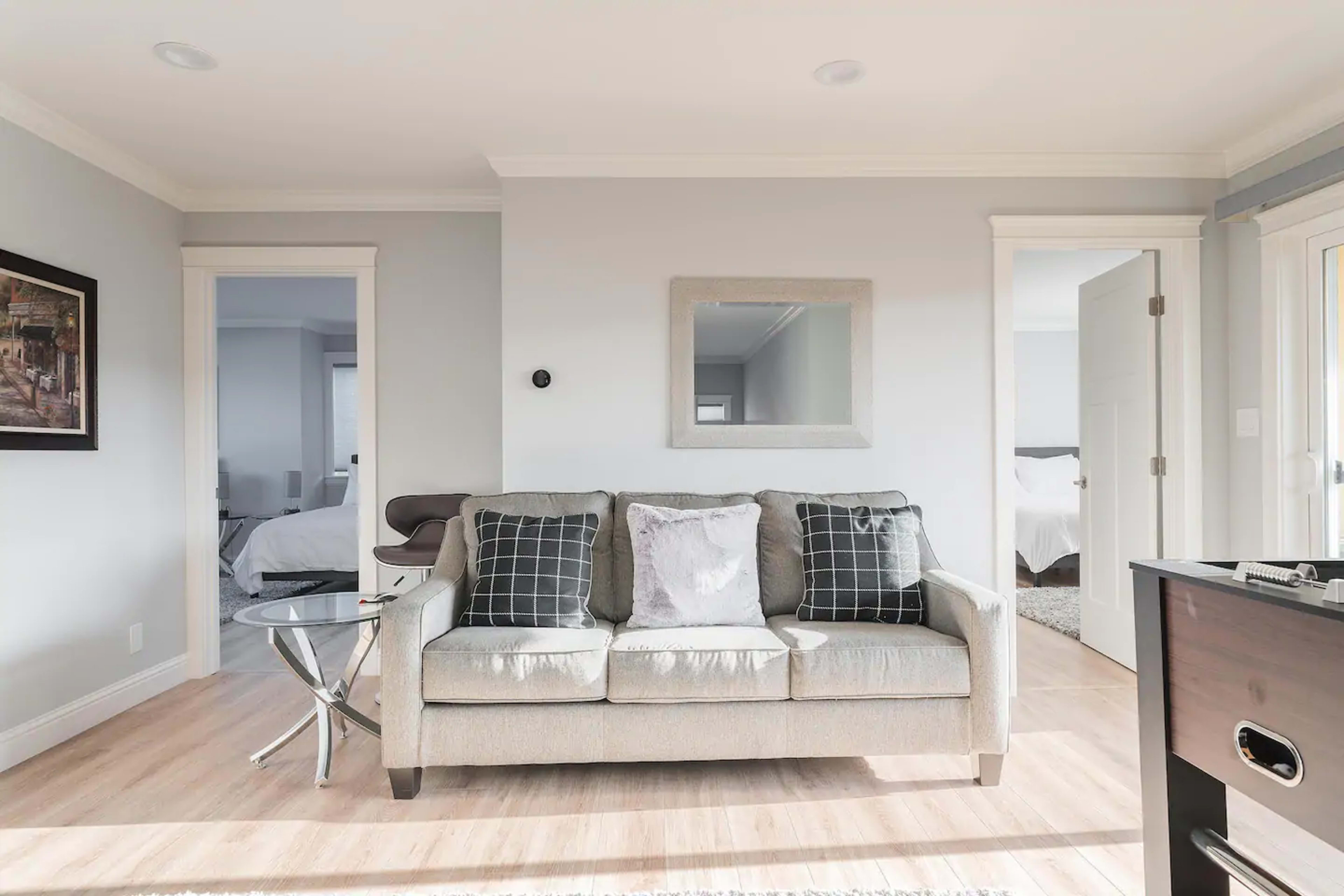 A light-colored couch with cushions sits in a bright, minimalist room featuring two doorways and a round side table.