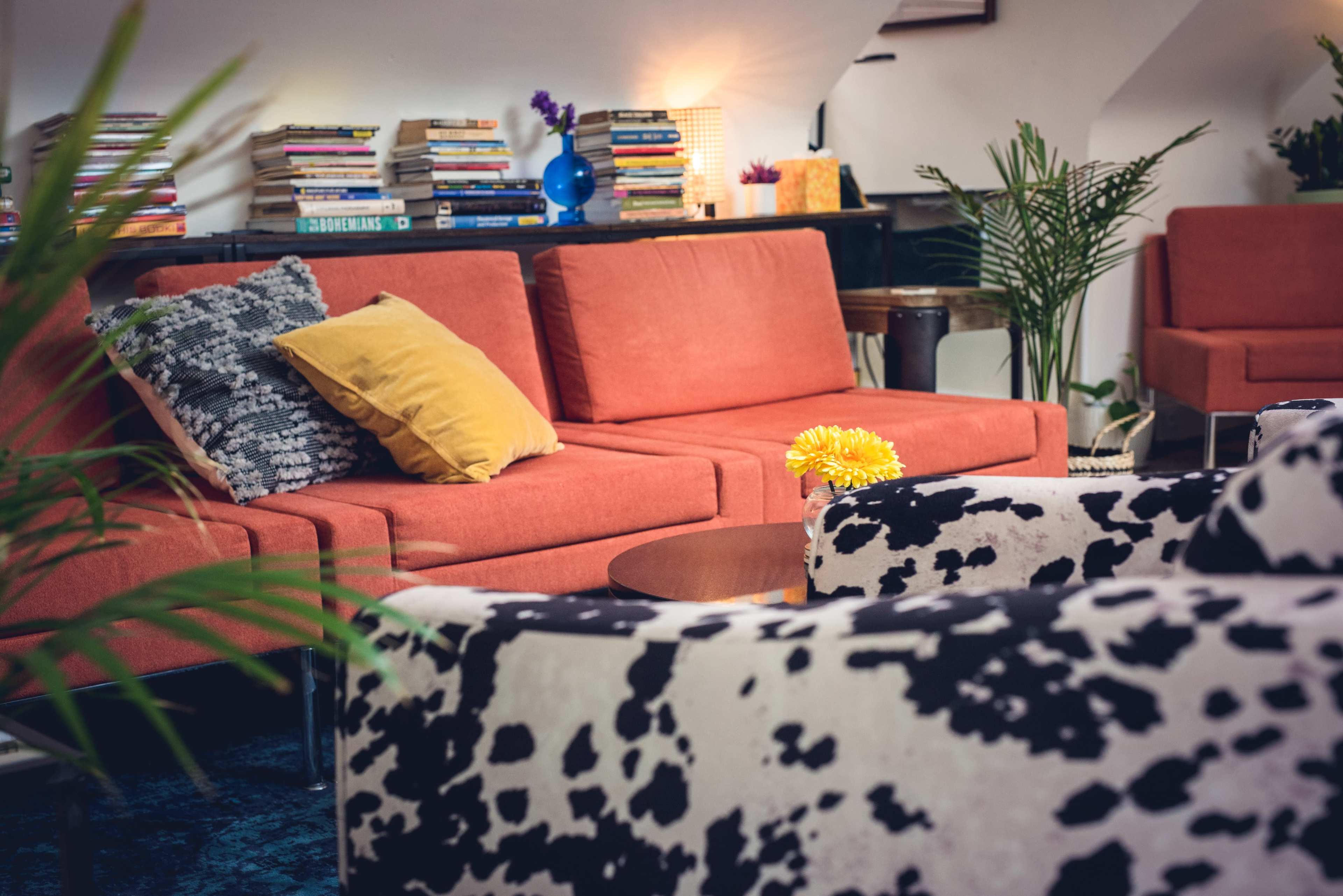 A modern living room featuring an orange sectional sofa, patterned chairs, a round coffee table, and shelves lined with books.