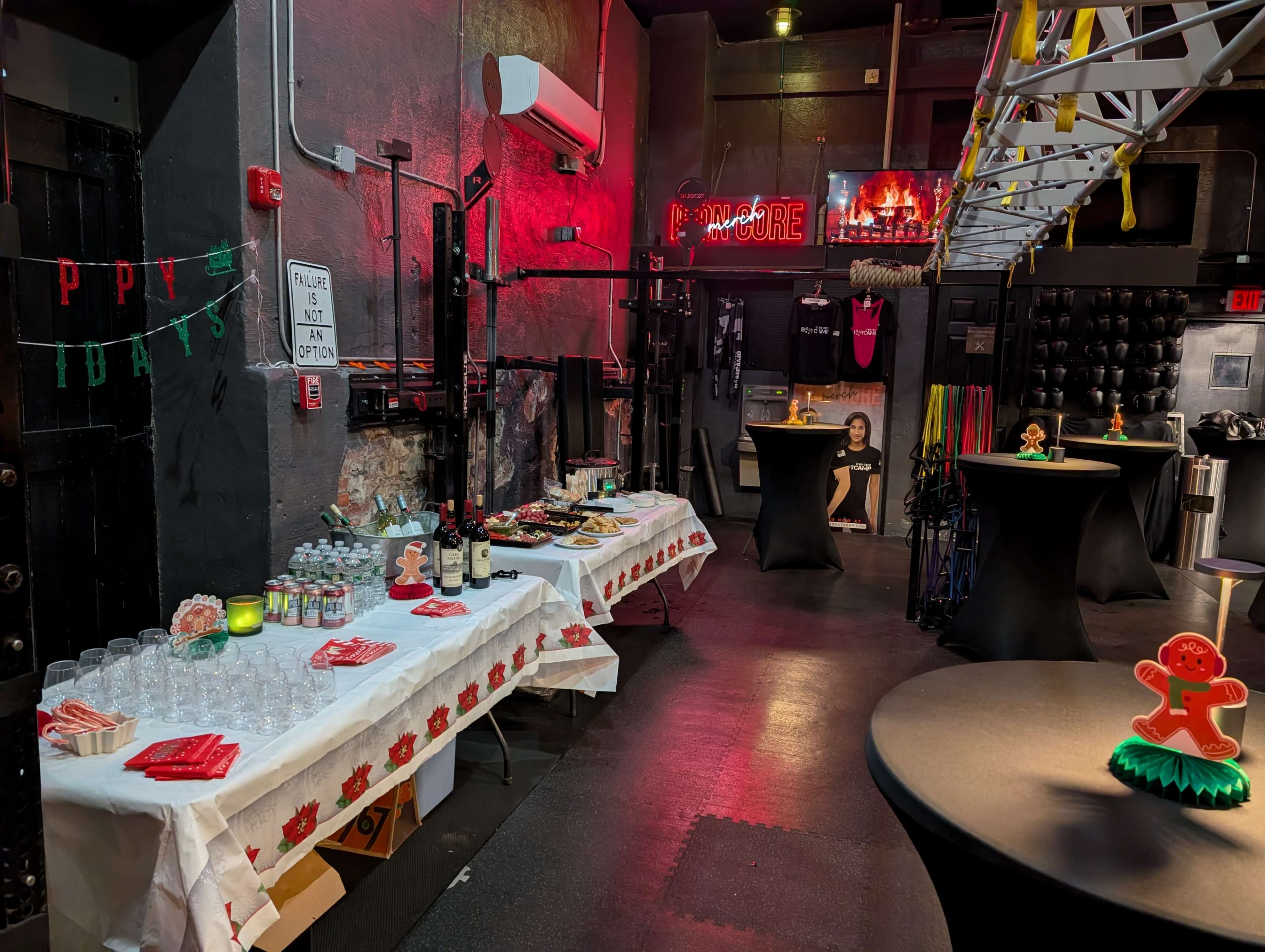 The image depicts a decorated event space with tables set up for refreshments, including drinks and snacks, alongside fitness equipment and decorations in a festive theme.