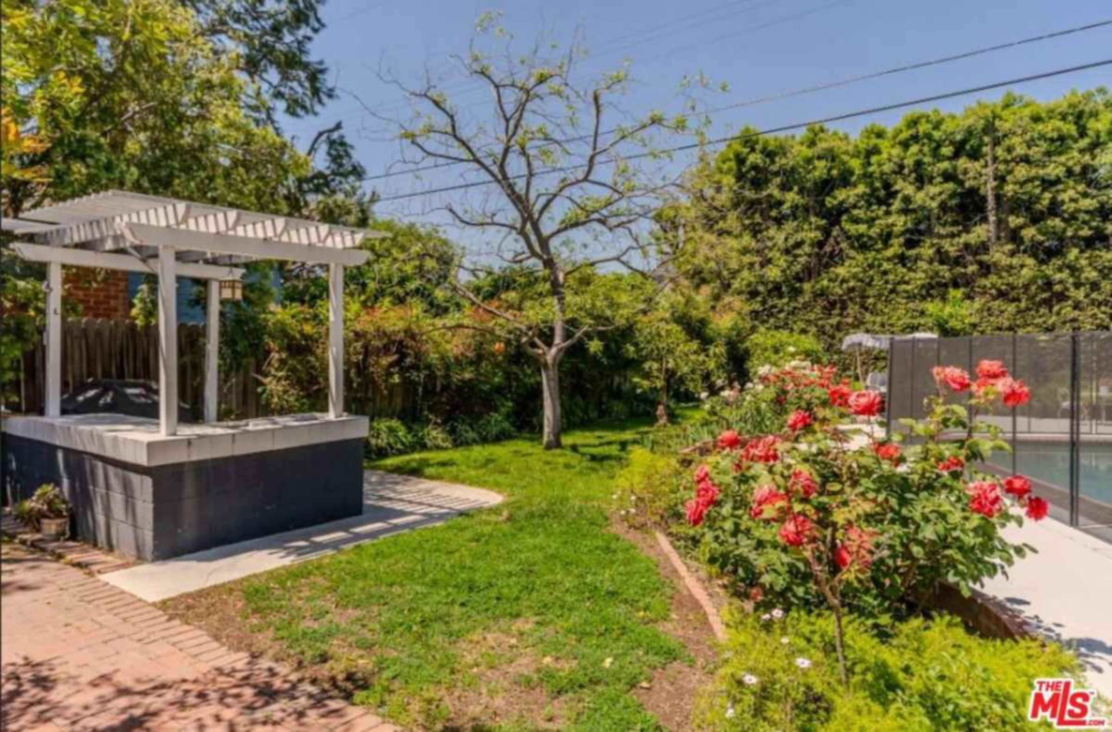 A backyard with a gazebo, a flowering garden, and a fenced swimming pool area.