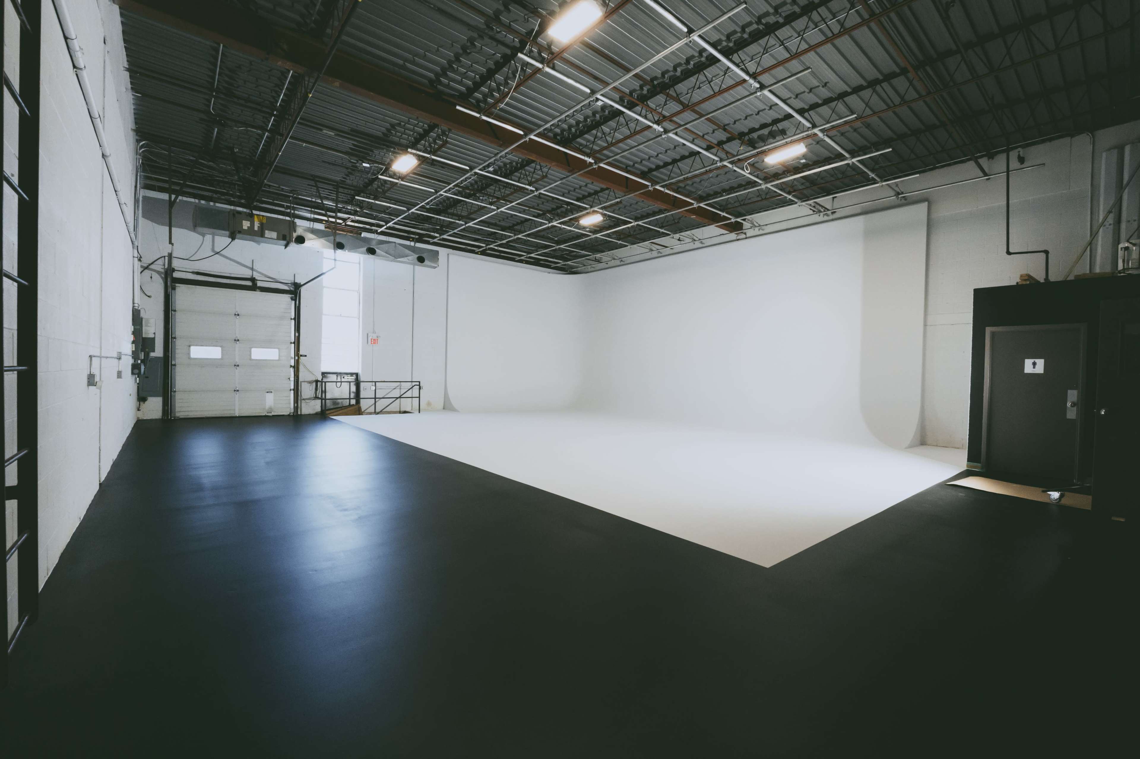 A spacious studio with a white seamless backdrop, concrete flooring, and overhead lighting.