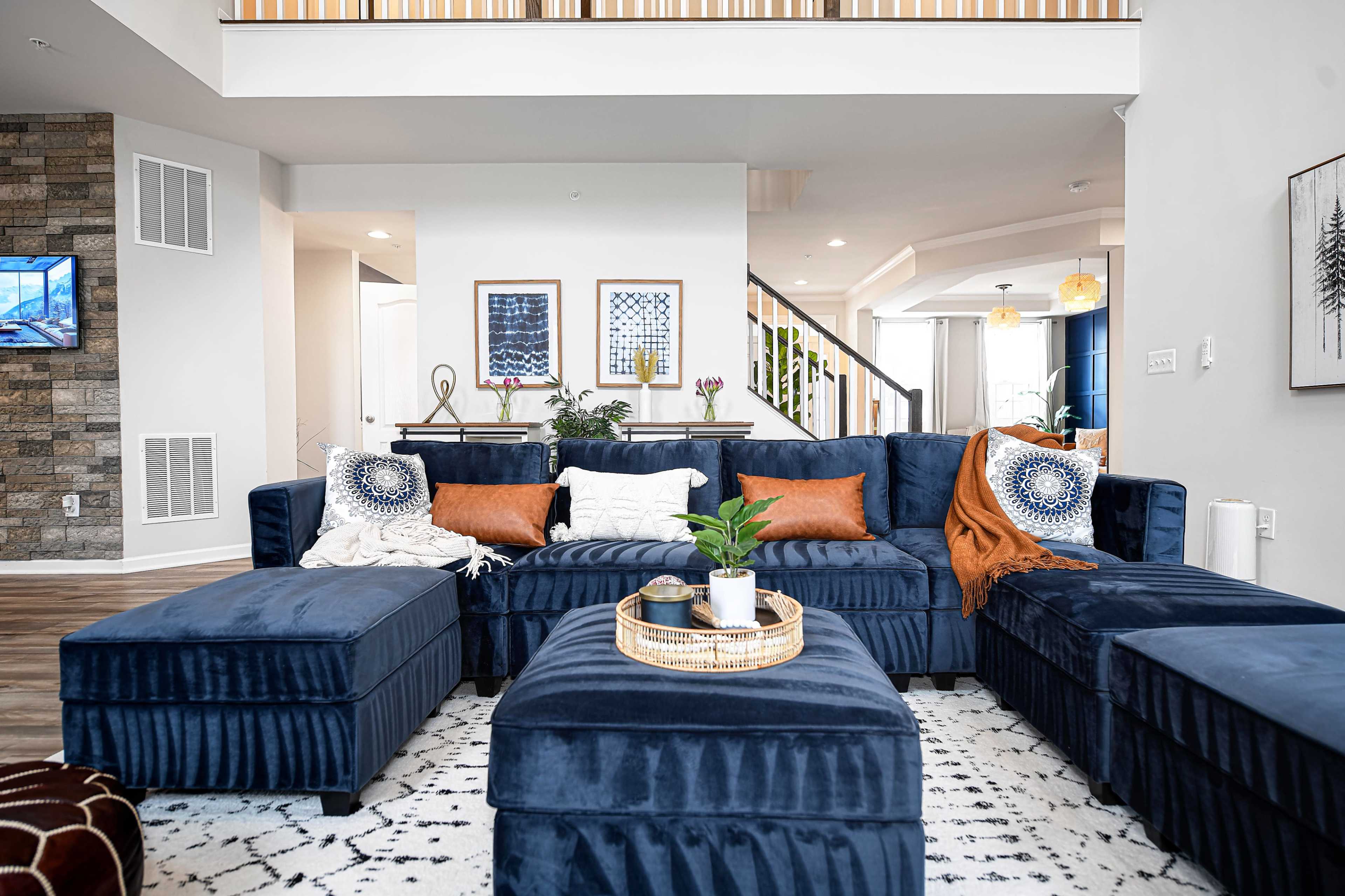 The image shows a modern living room with a dark blue sectional sofa arranged around a round coffee table on a patterned rug.