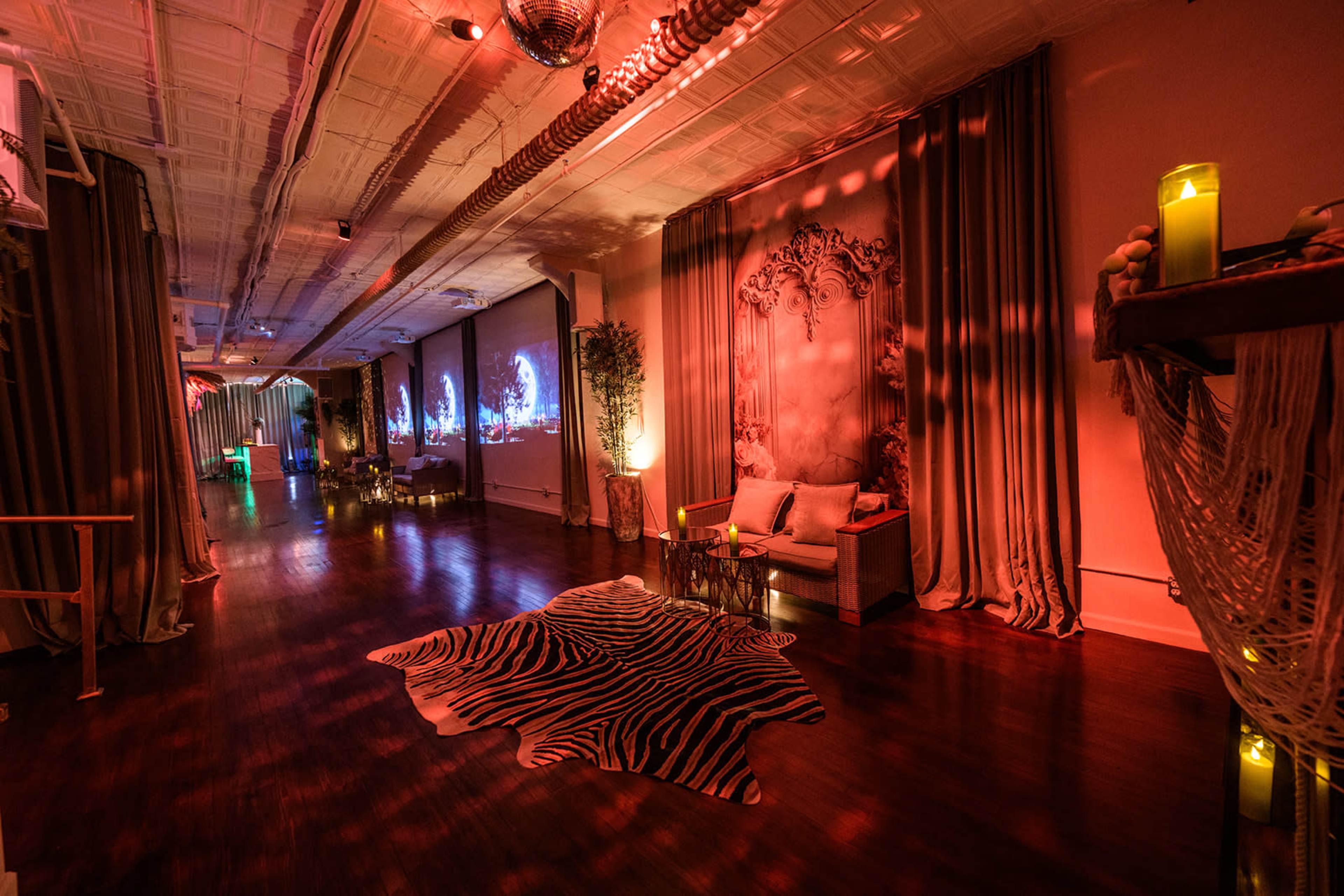 The image shows a spacious room with wooden flooring, featuring decorative curtains, a projected display on the wall, and ambient lighting creating a warm atmosphere.