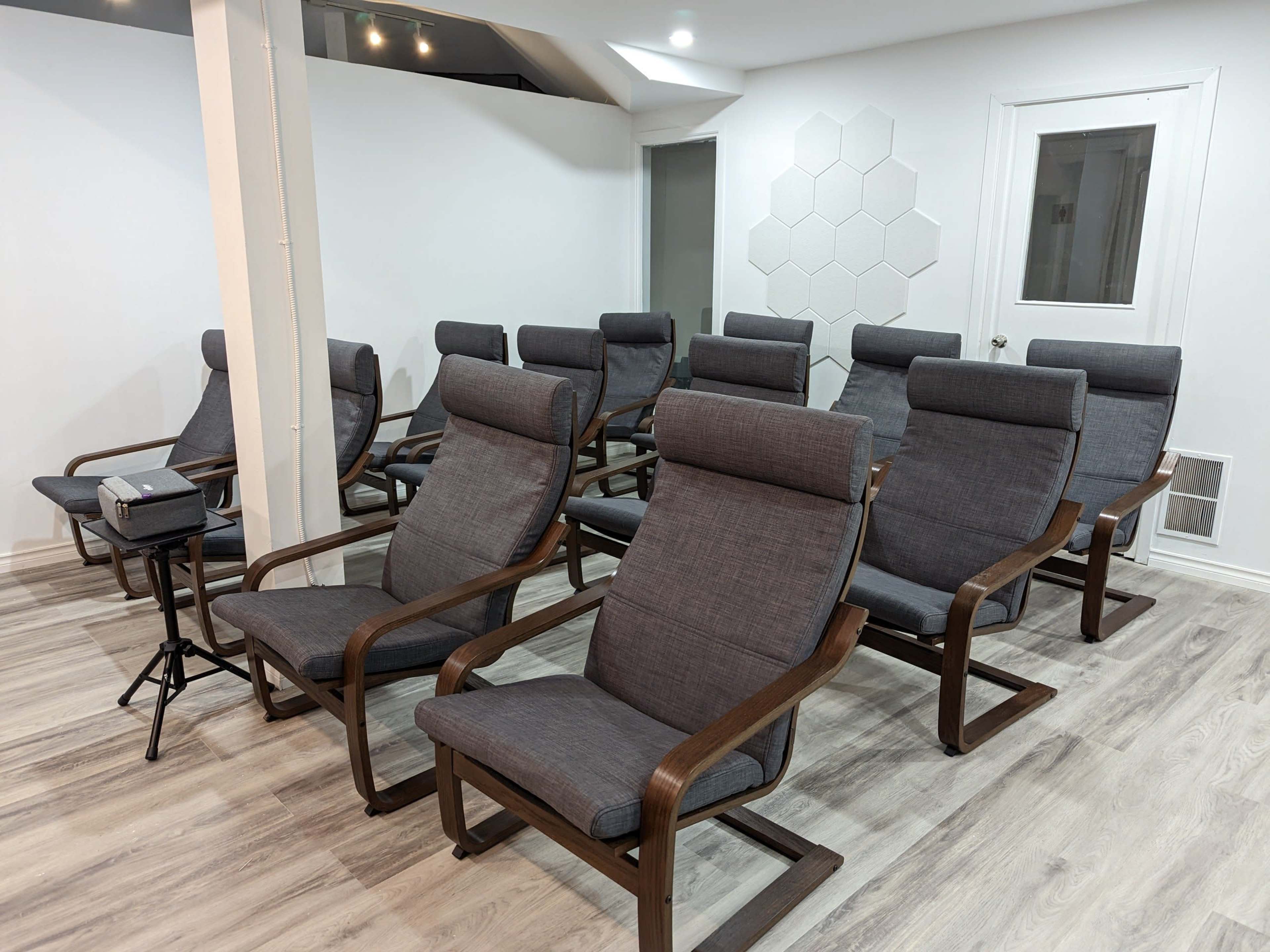 A row of grey reclining chairs arranged in a well-lit room with a white wall and hexagonal paneling.
