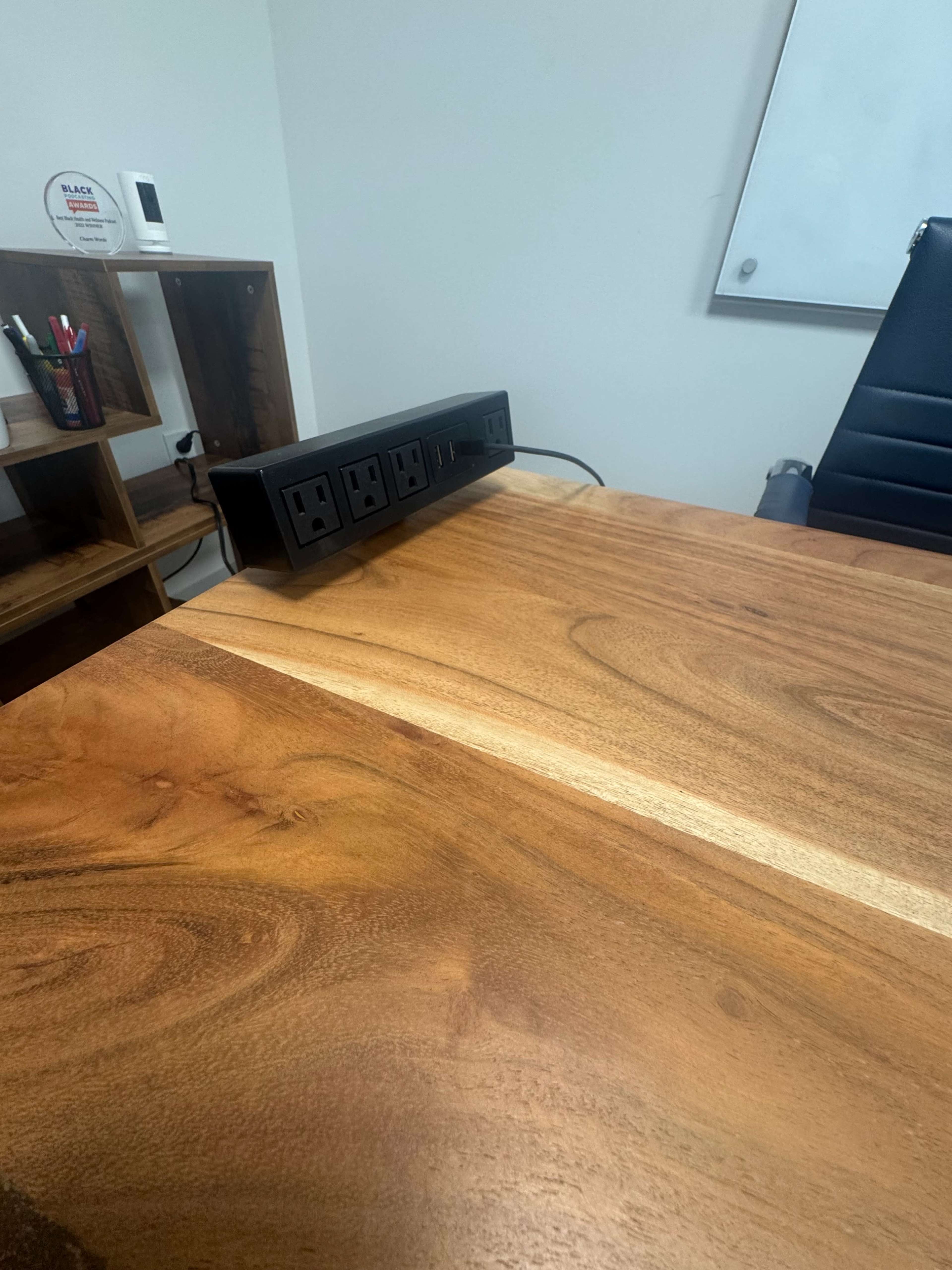 A wooden desk with a power strip and office supplies in the background is shown in an office setting.
