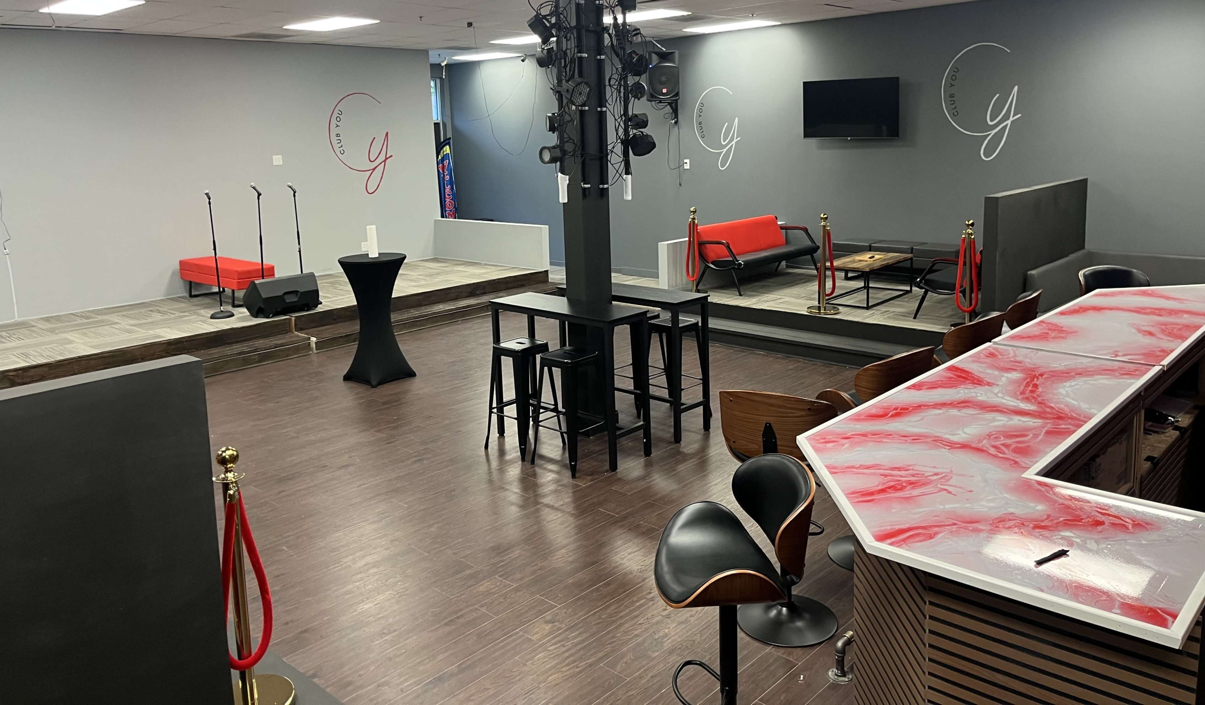 The image shows a performance space with a small stage, seating area, and a bar counter, featuring a sleek design and modern furnishings.