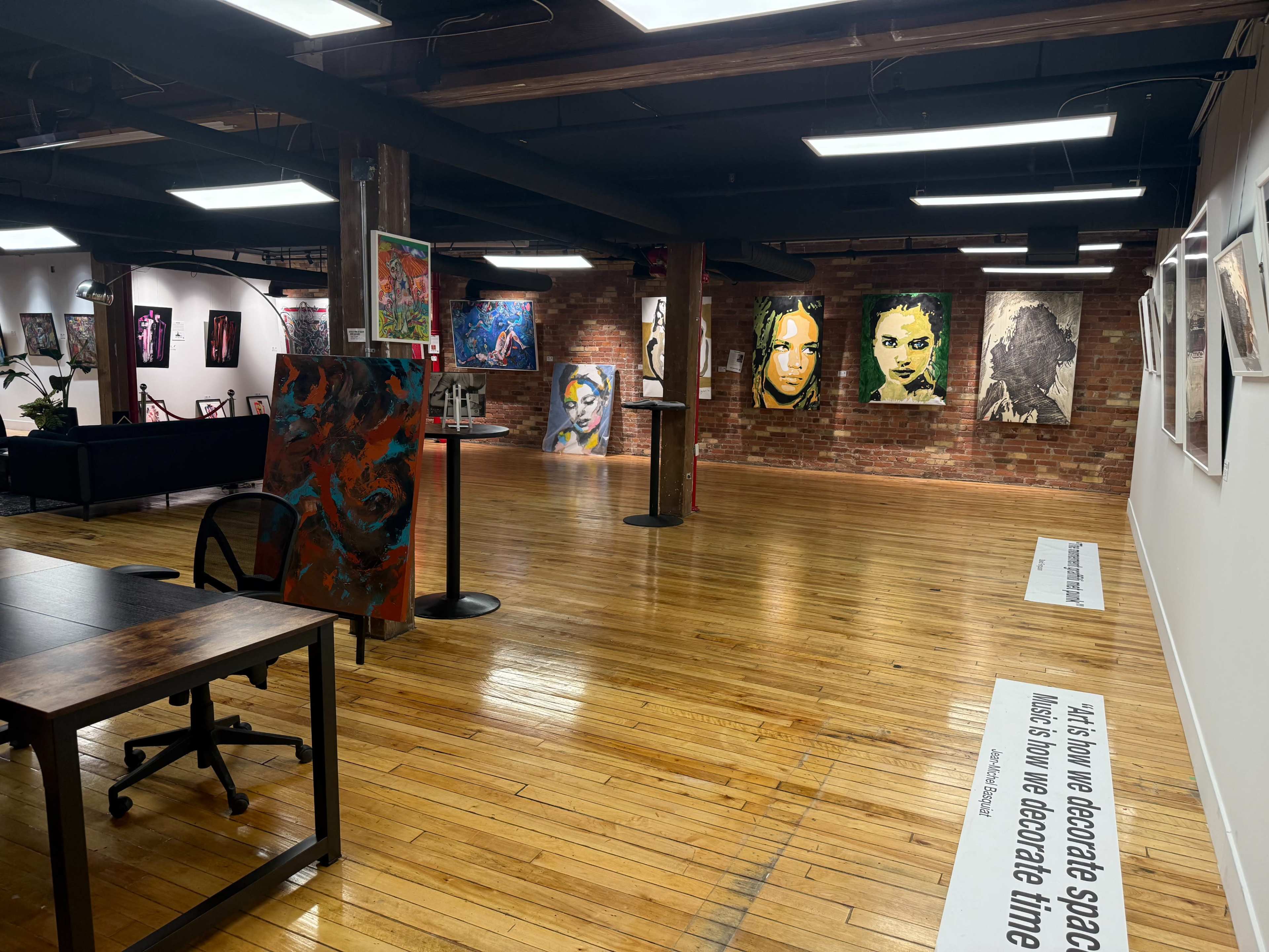 The image shows an art gallery with various framed artworks on the walls and a wooden floor, highlighting a mixture of paintings and photographs.