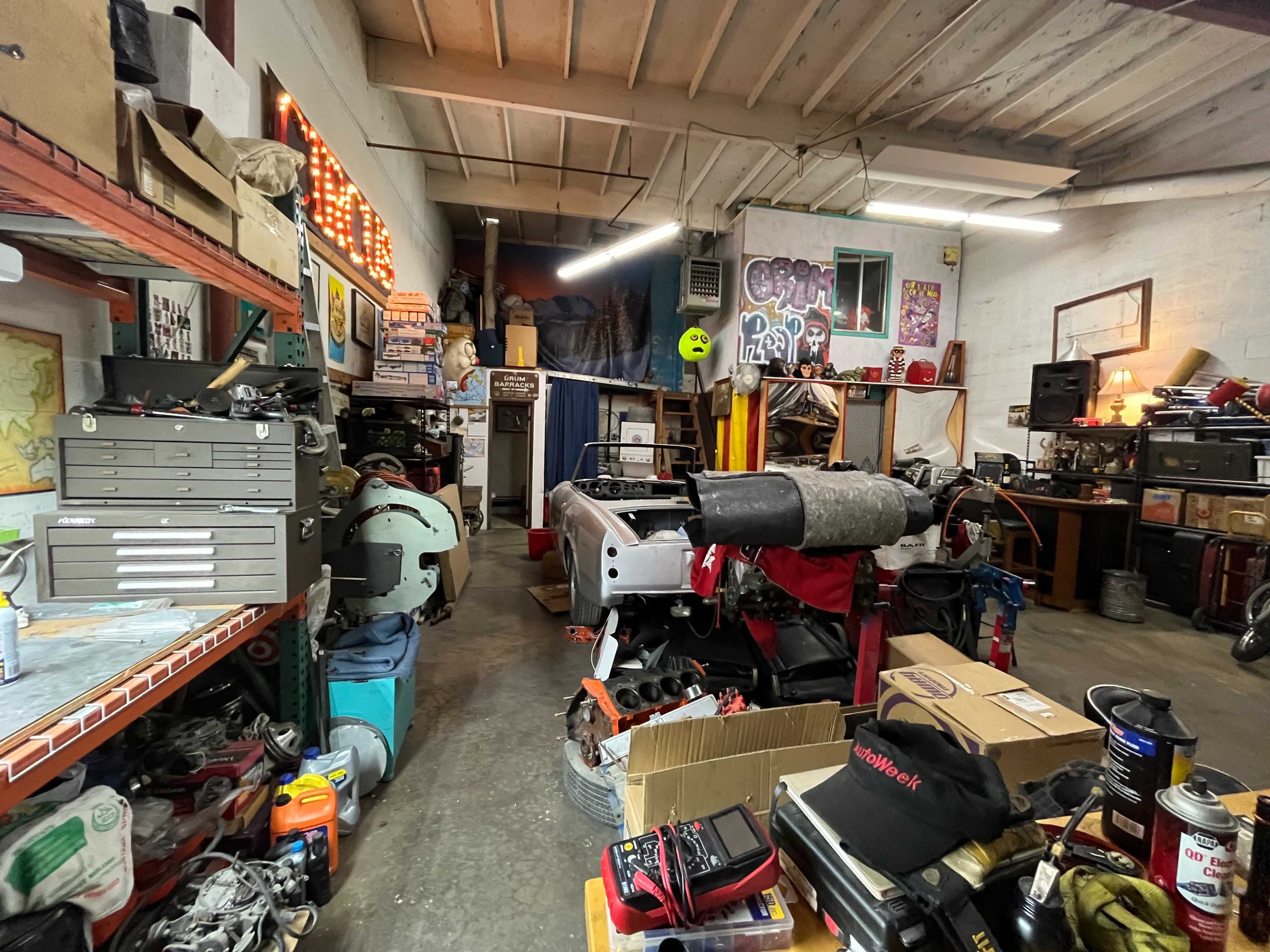 A cluttered garage workshop filled with various tools, equipment, and automotive parts.