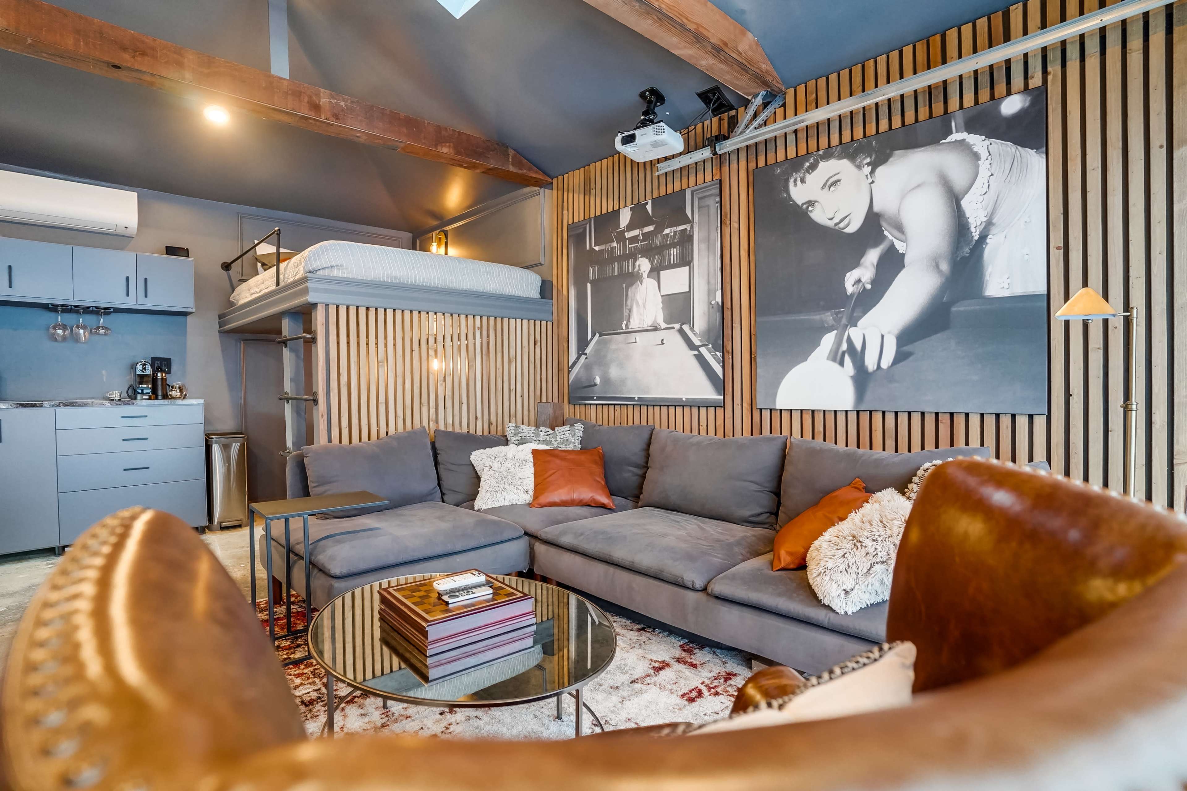 A modern living area featuring a gray sectional sofa, a glass coffee table, and framed black-and-white photographs on a wood-paneled wall.