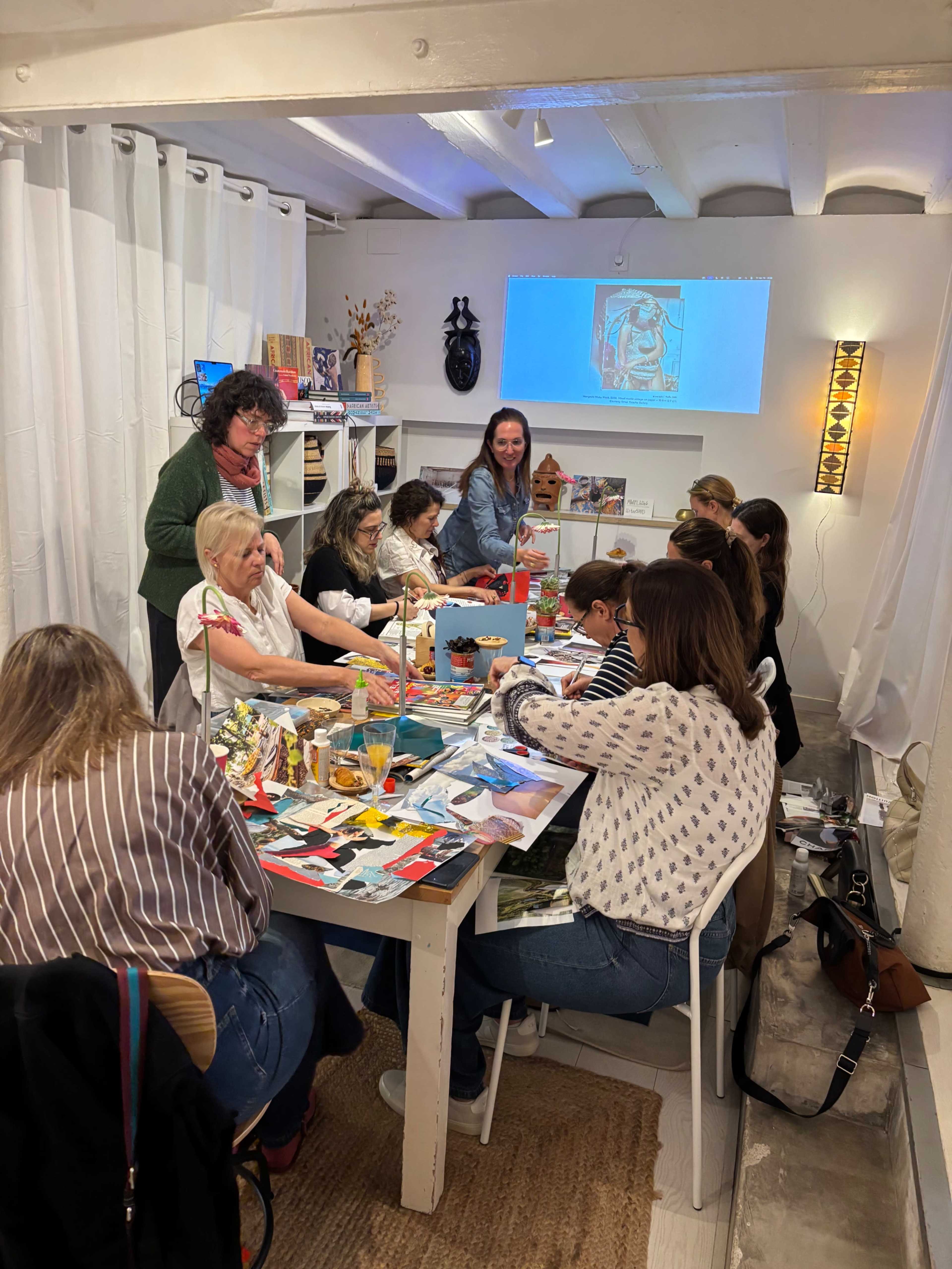 A group of women are engaged in a creative workshop around a large table filled with art supplies and projects in a well-lit room.