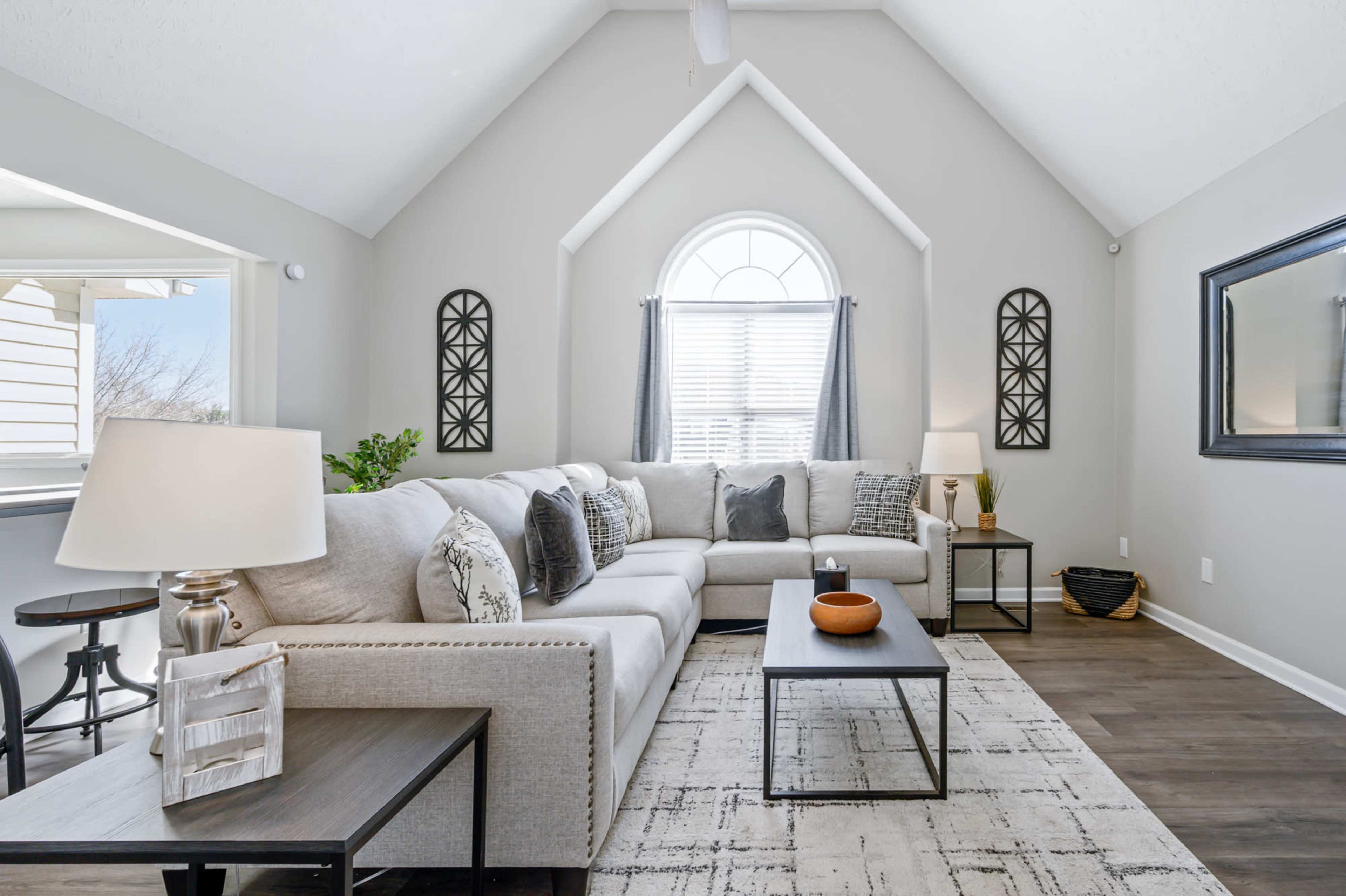 The living room features a large sectional sofa, a coffee table, and large windows with natural light, creating an open and inviting atmosphere.