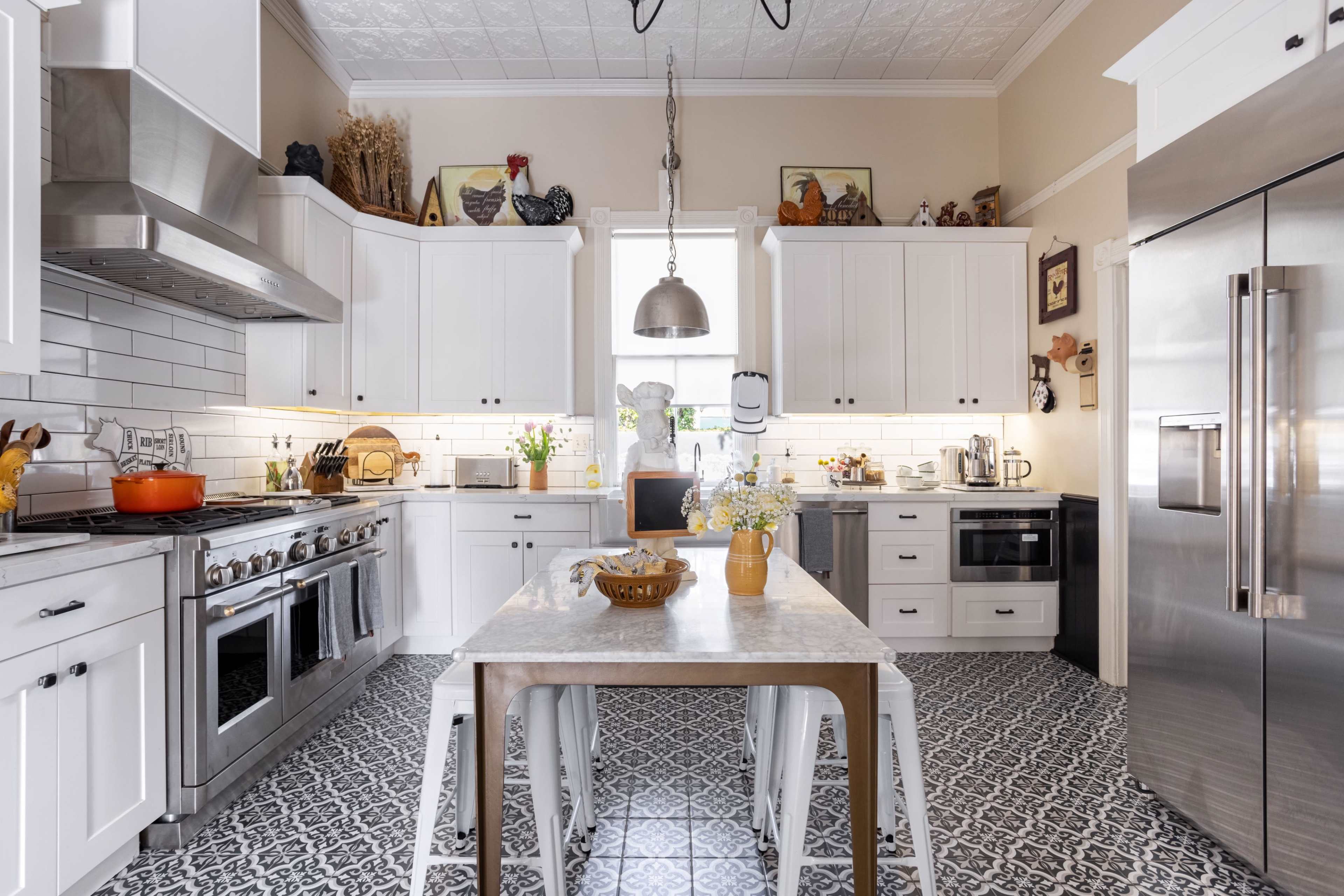 A modern kitchen features white cabinetry, stainless steel appliances, a central island with a marble top, and decorative tile flooring.