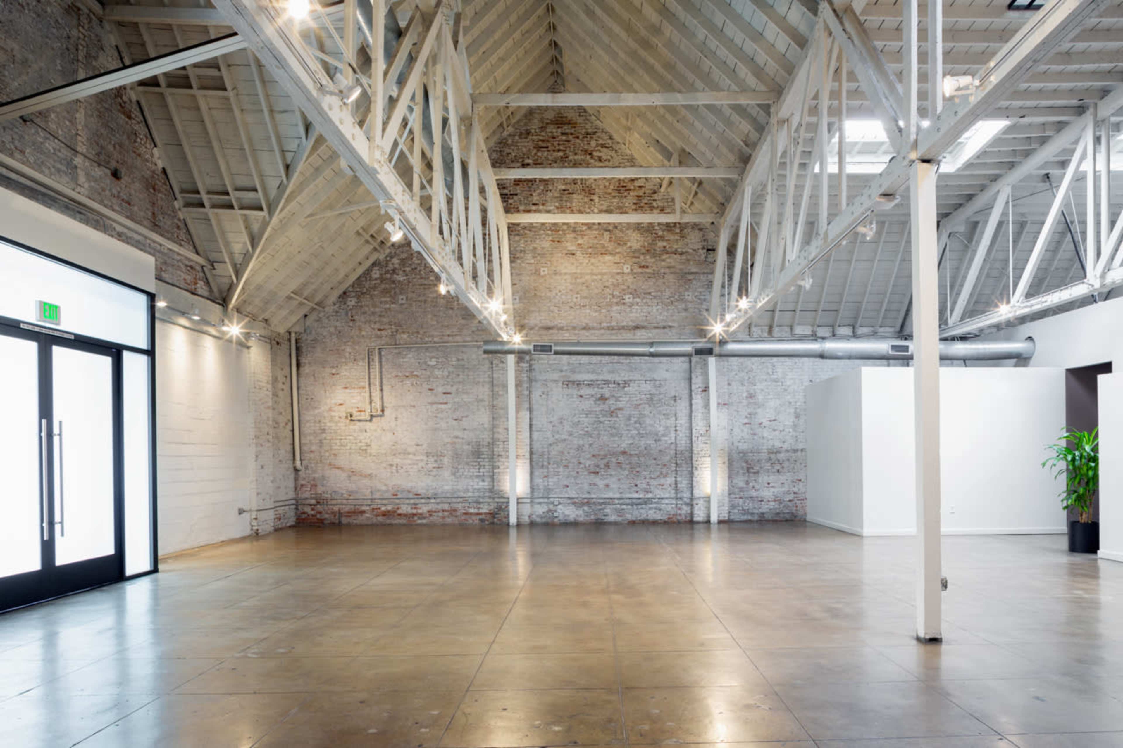 The image features a spacious, industrial-style interior with exposed brick walls, high ceilings, and polished concrete flooring.