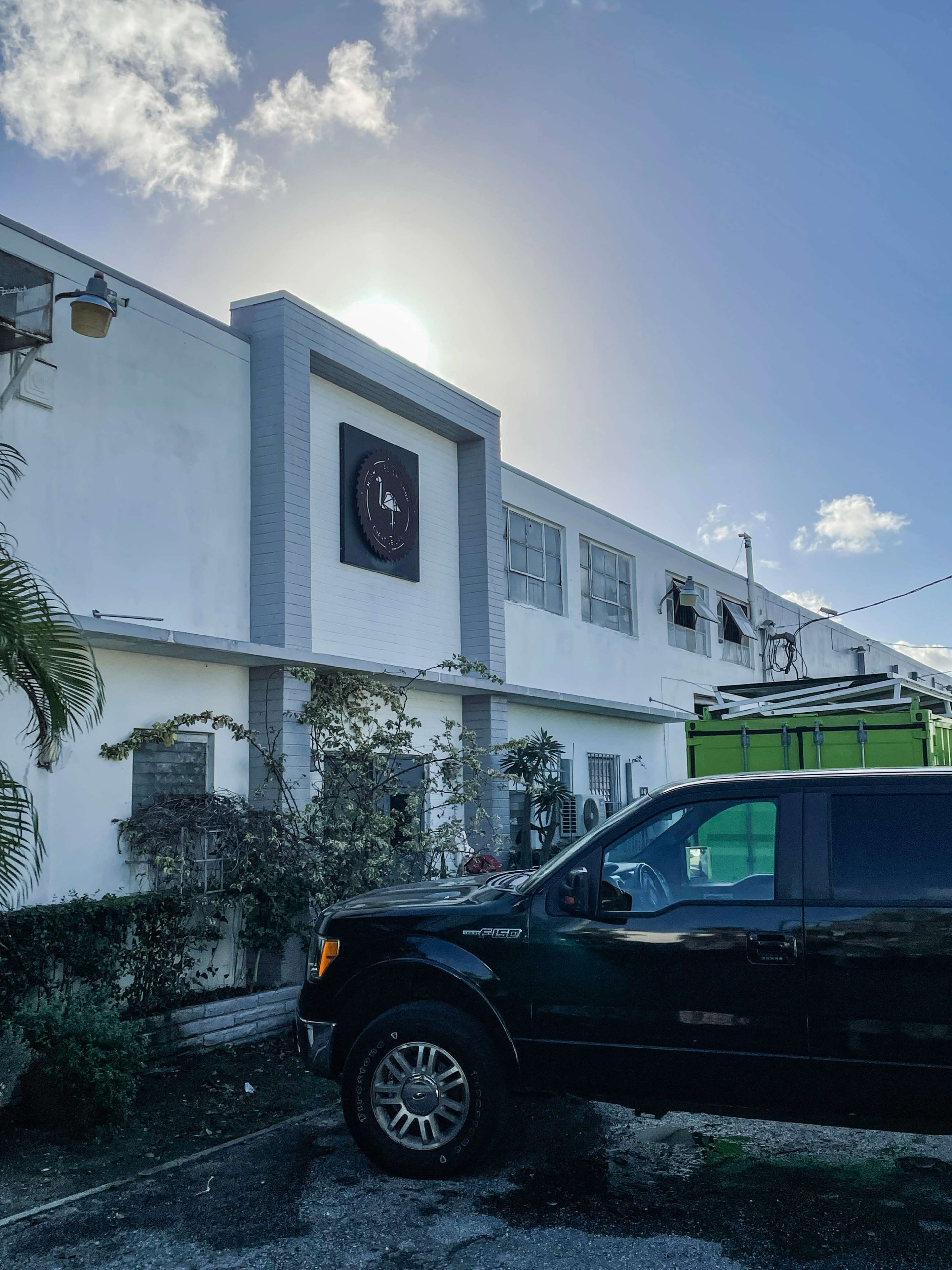A black truck is parked in front of a white building with a sign and windows, under a clear blue sky.