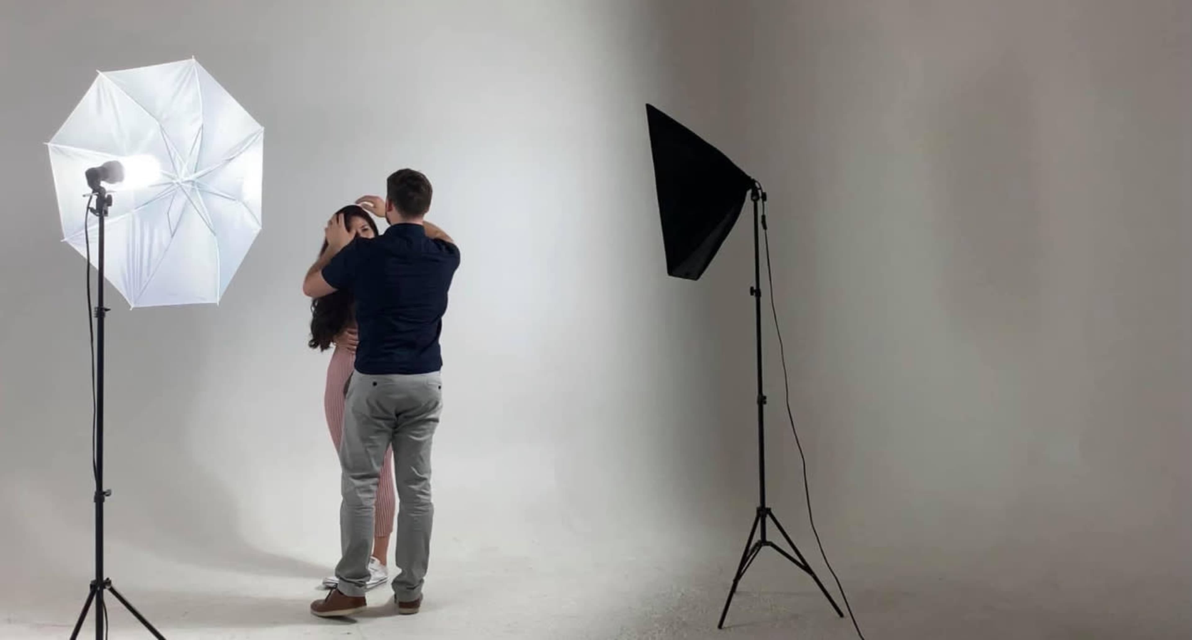 A man and a woman are posing closely together in a photography studio with softbox lights on either side.