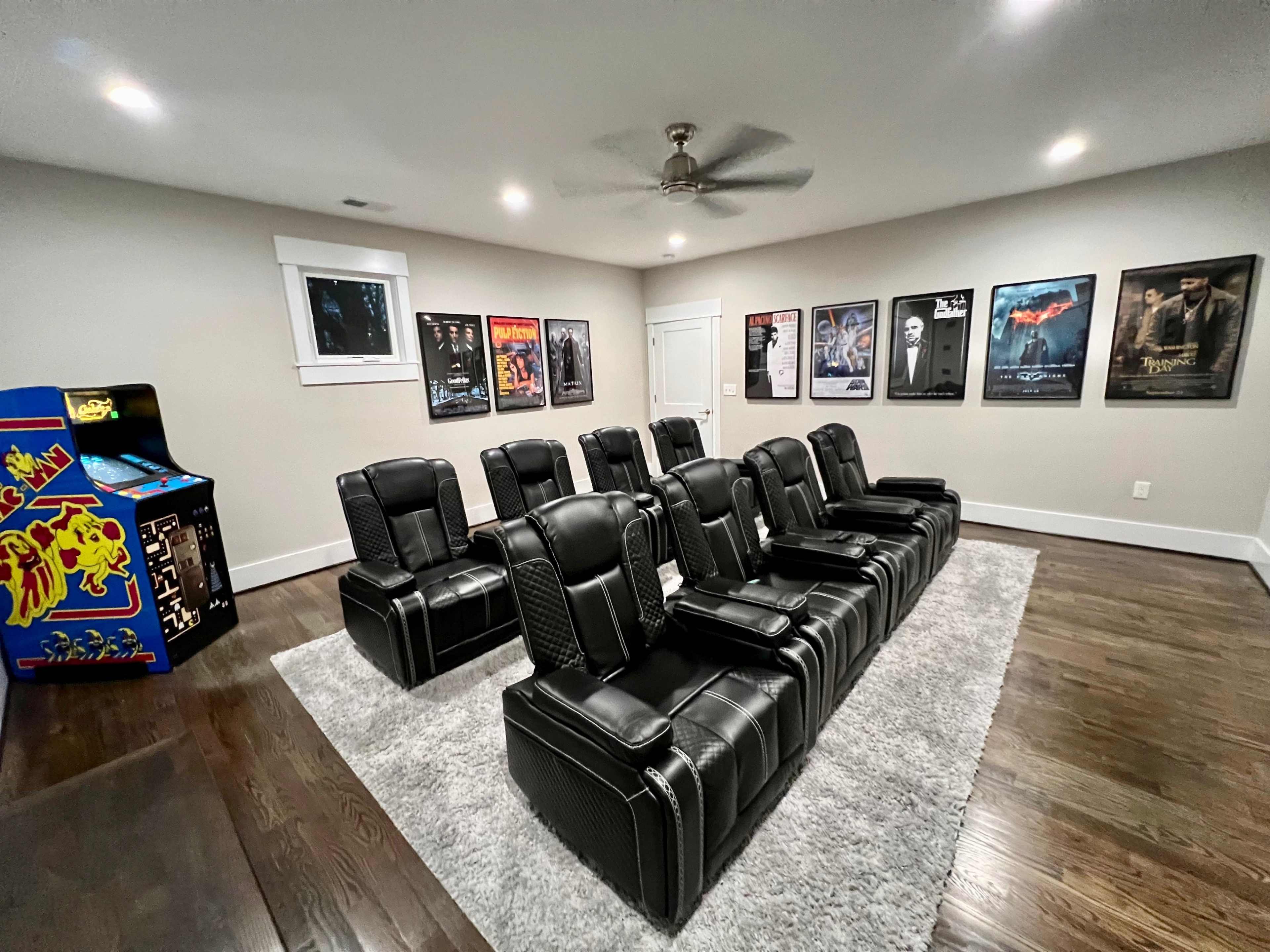 The room features a row of black reclining theater seats arranged in front of framed movie posters, with an arcade machine in the corner.