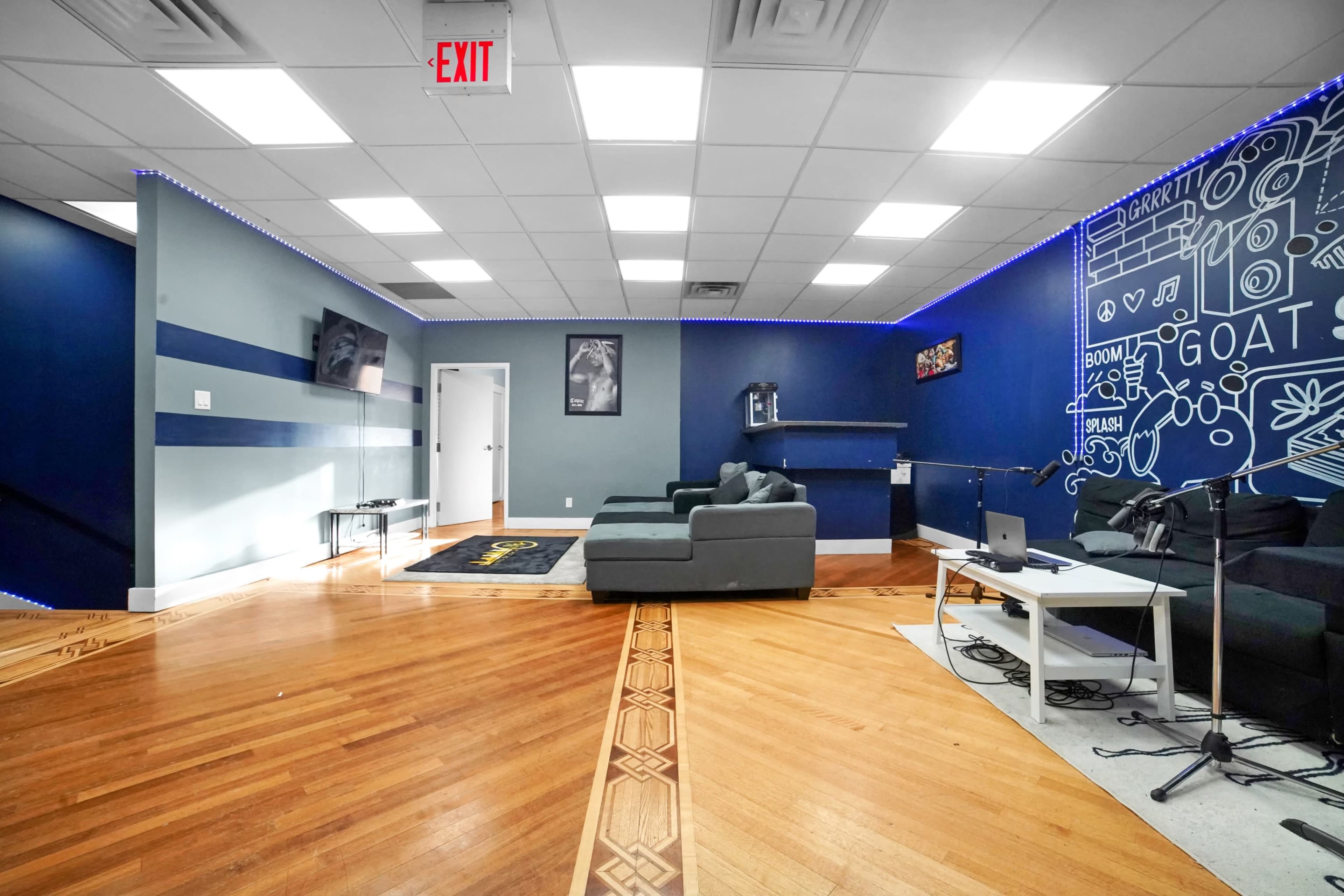 A modern lounge area with dark blue walls, hardwood flooring, and furniture including a gray sofa, a white table, and a television mounted on the wall.