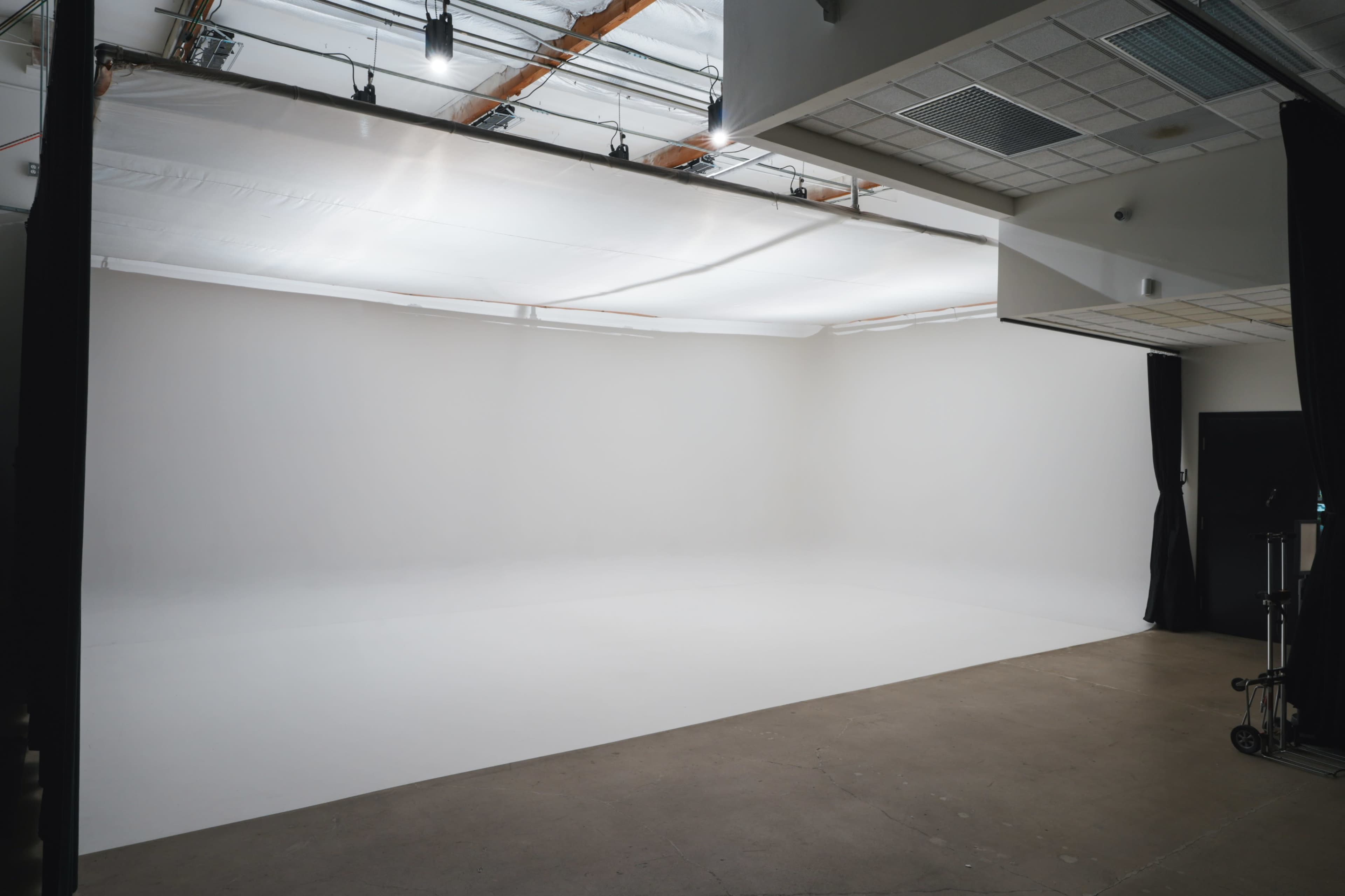 The image shows a spacious, empty studio with a seamless white backdrop and a smooth floor.