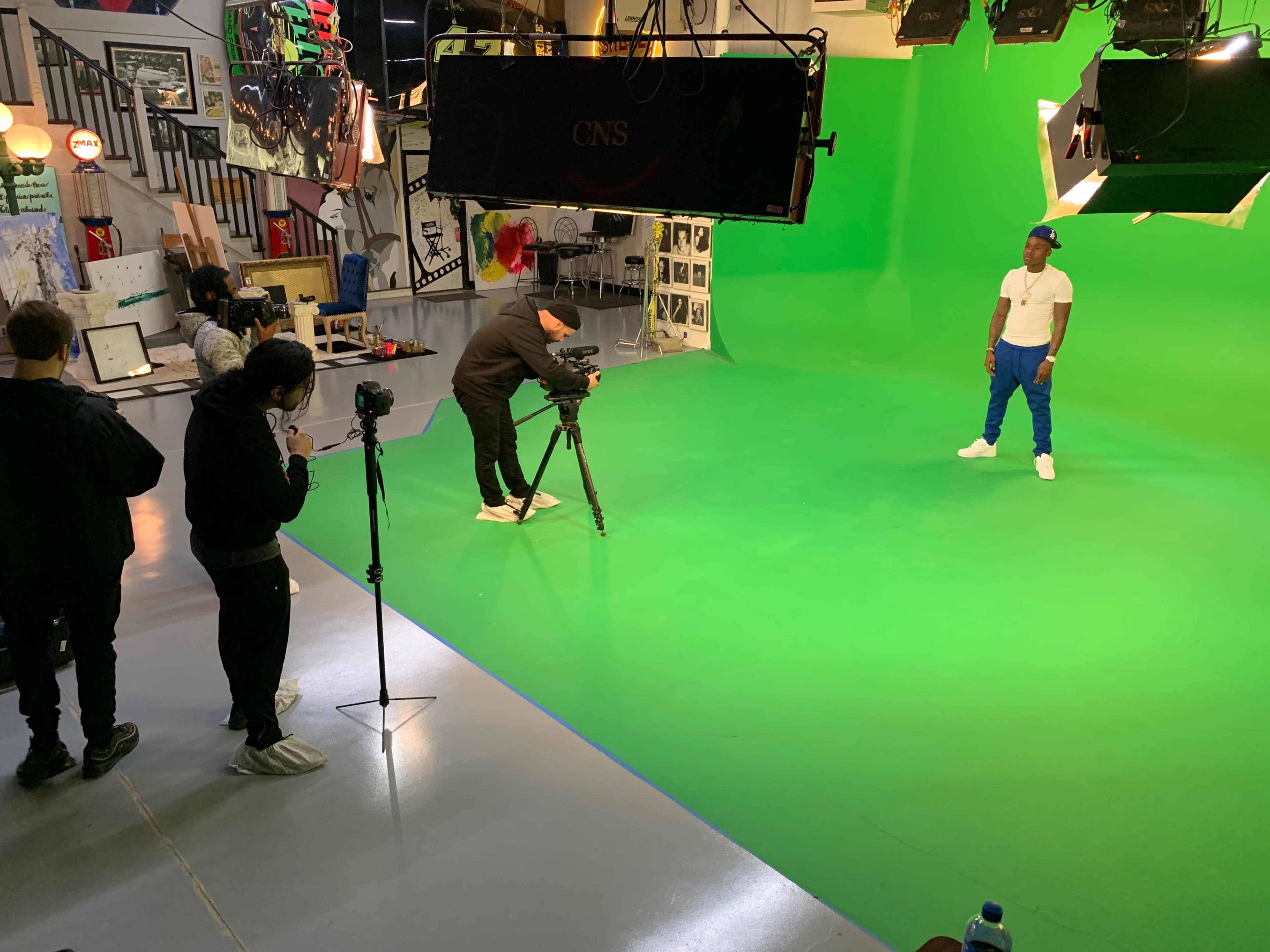 A film crew sets up equipment and prepares to shoot a scene with an actor on a green screen backdrop.