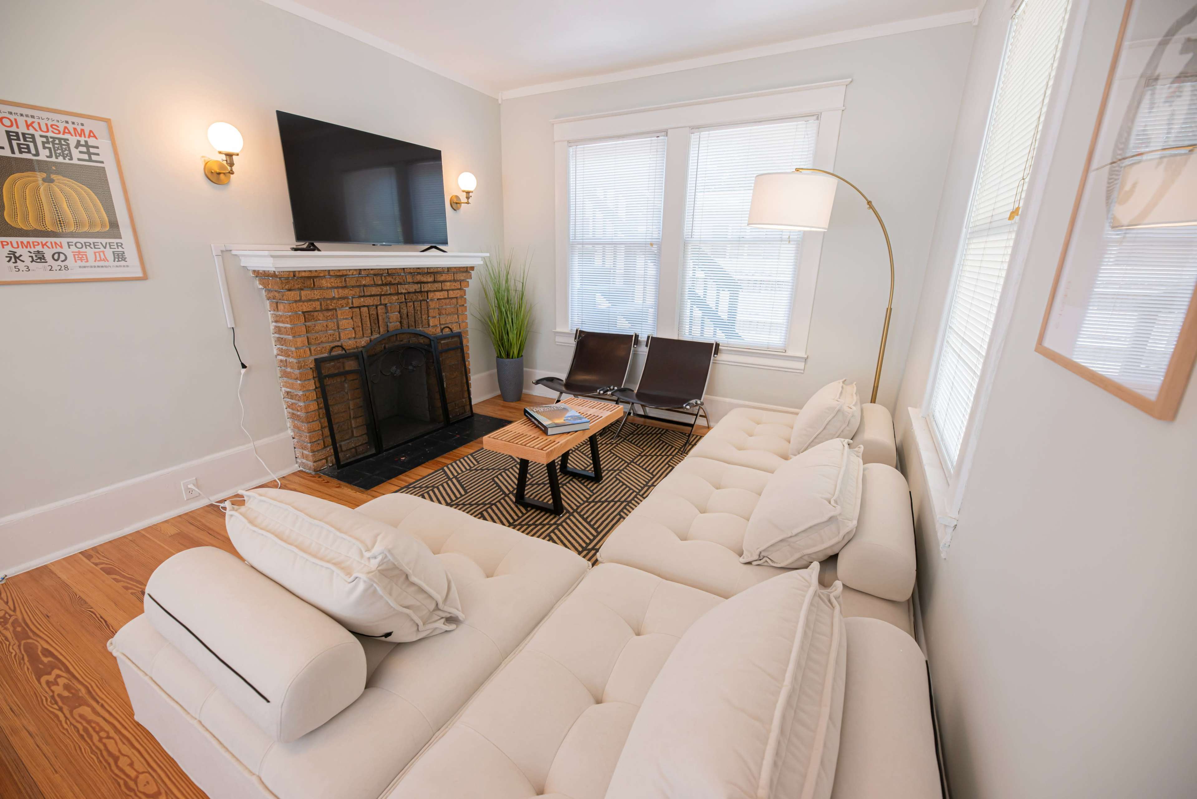 A living room featuring a sectional sofa, a TV mounted above a brick fireplace, and two lounge chairs beside a coffee table.