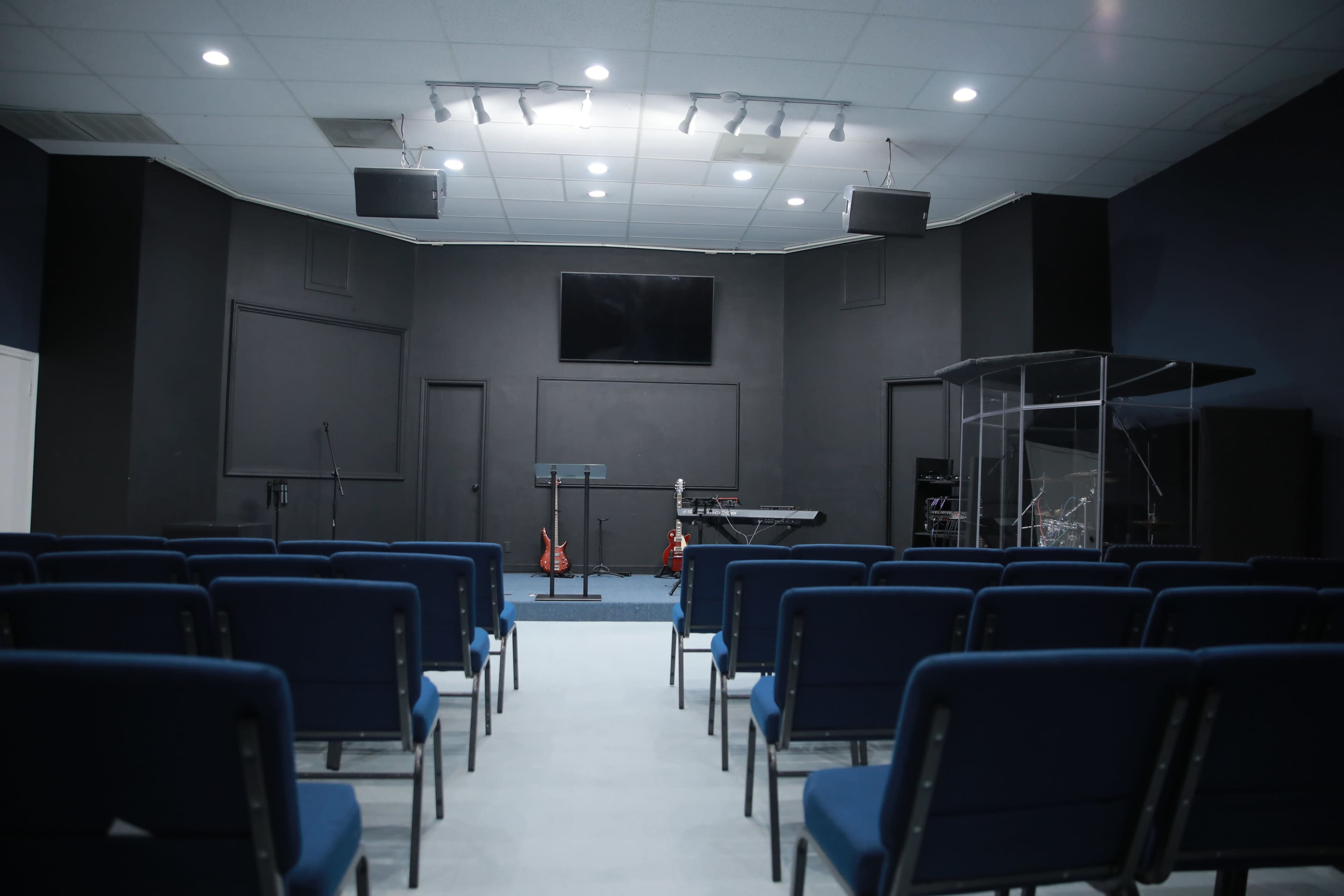 A music performance space with blue chairs facing a stage that features musical instruments and equipment.