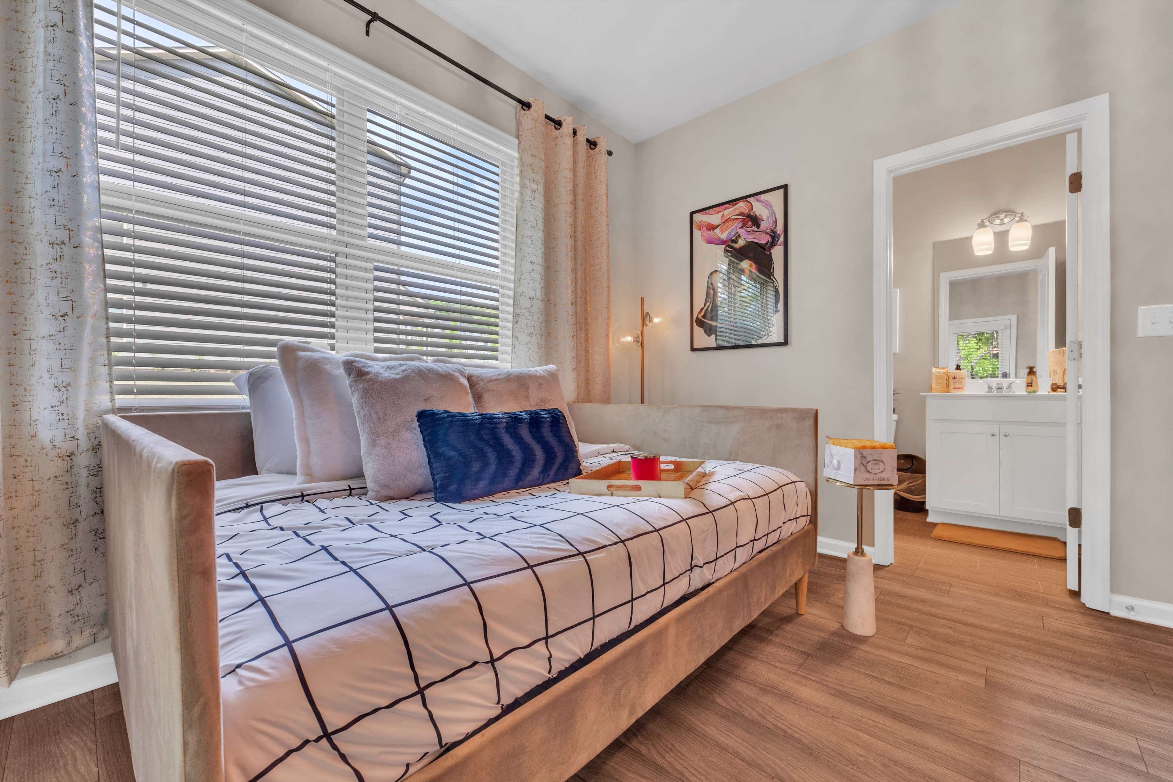 A bedroom featuring a daybed with decorative pillows, a window with blinds, and a view into a bathroom area through an open door.