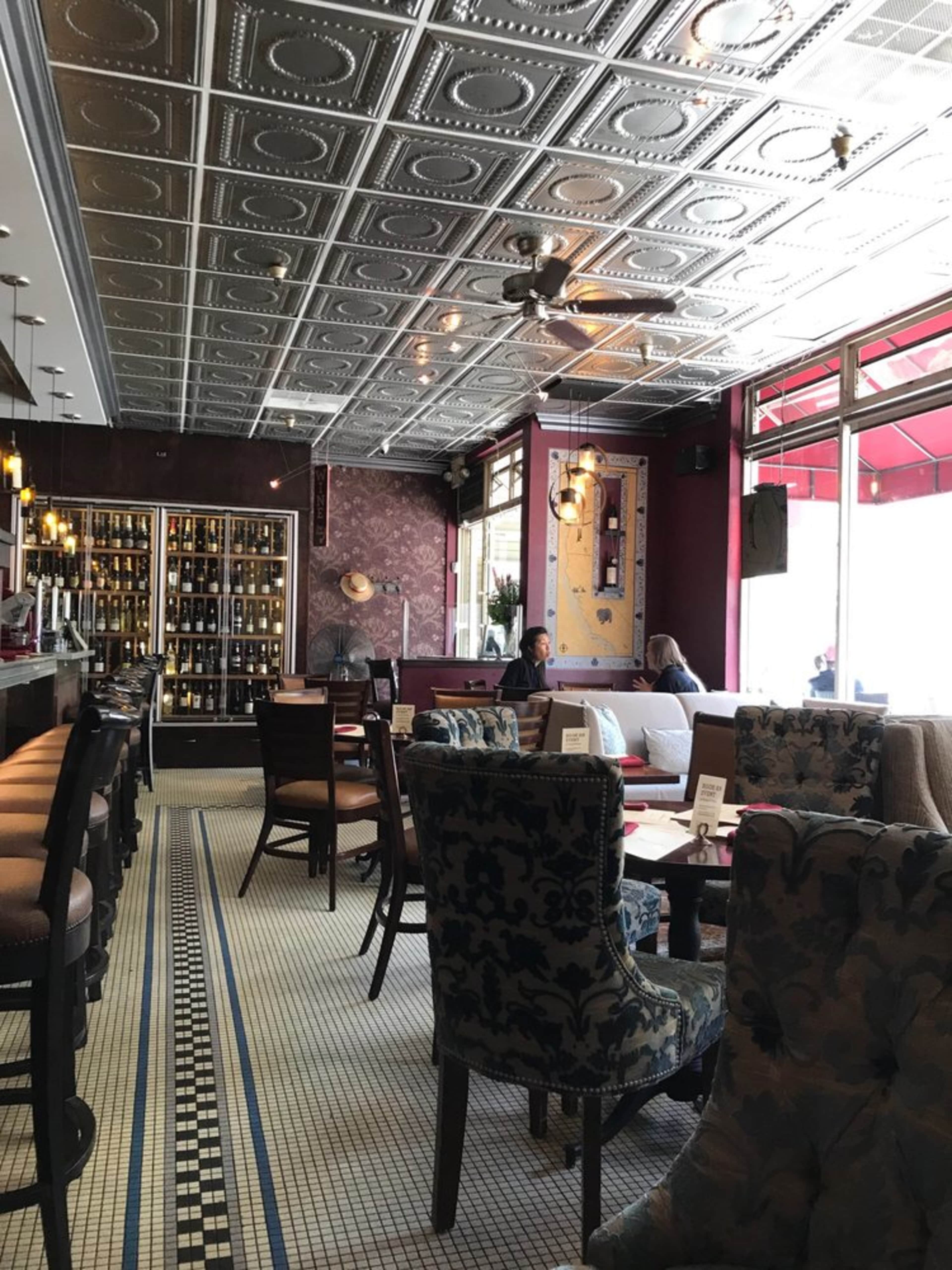 The interior of a restaurant featuring a patterned tile floor, a bar area with a wine display, and upholstered seating.