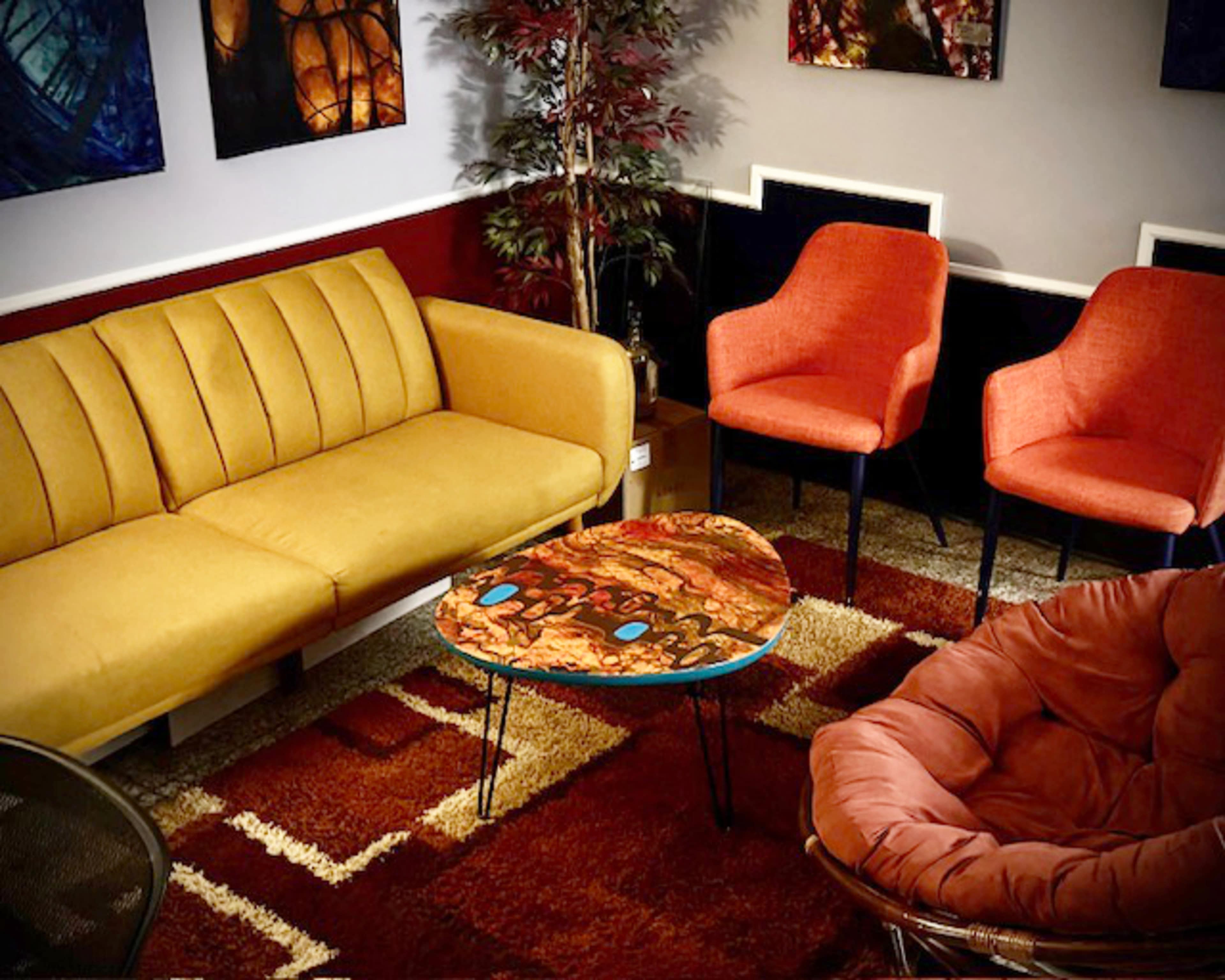 The living room scene features a yellow couch, two orange chairs, a round table with an abstract design, and a brown area rug.