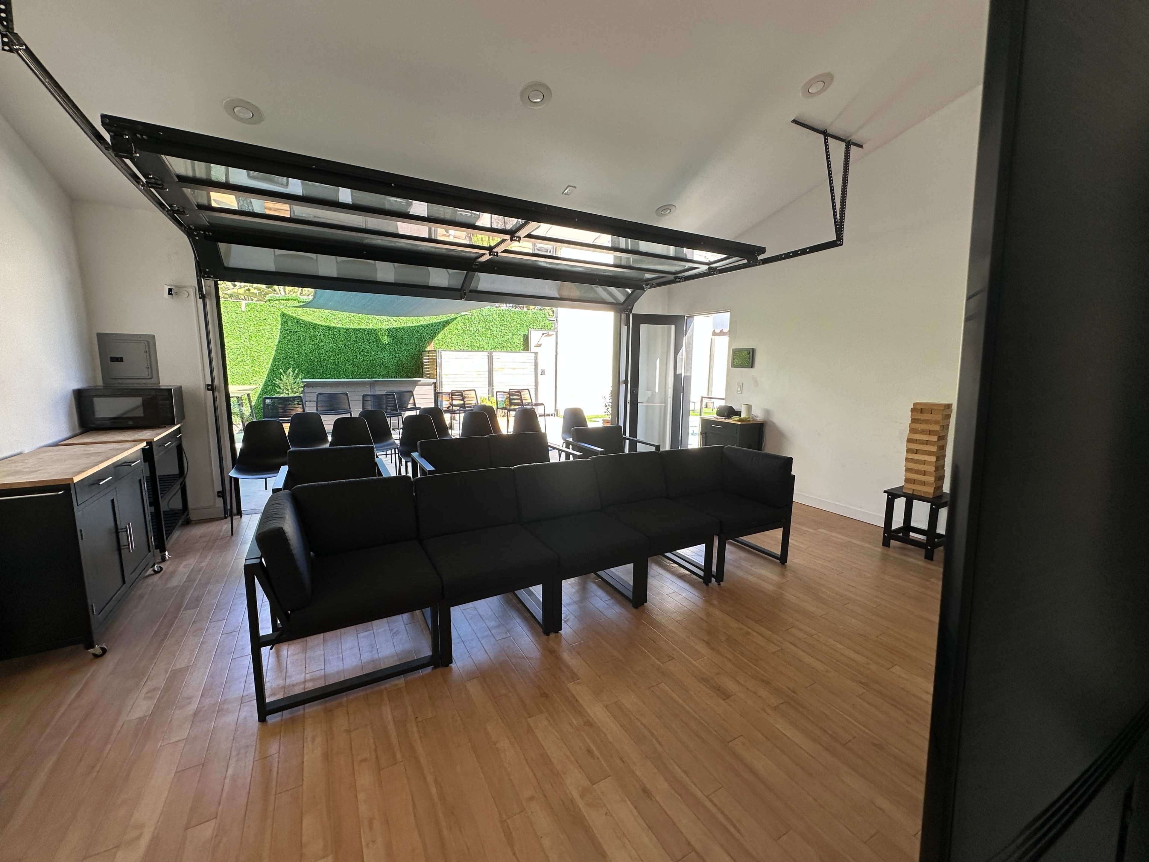 A modern interior space with a row of black seating arranged in front of a large open garage door that leads to an outdoor area.