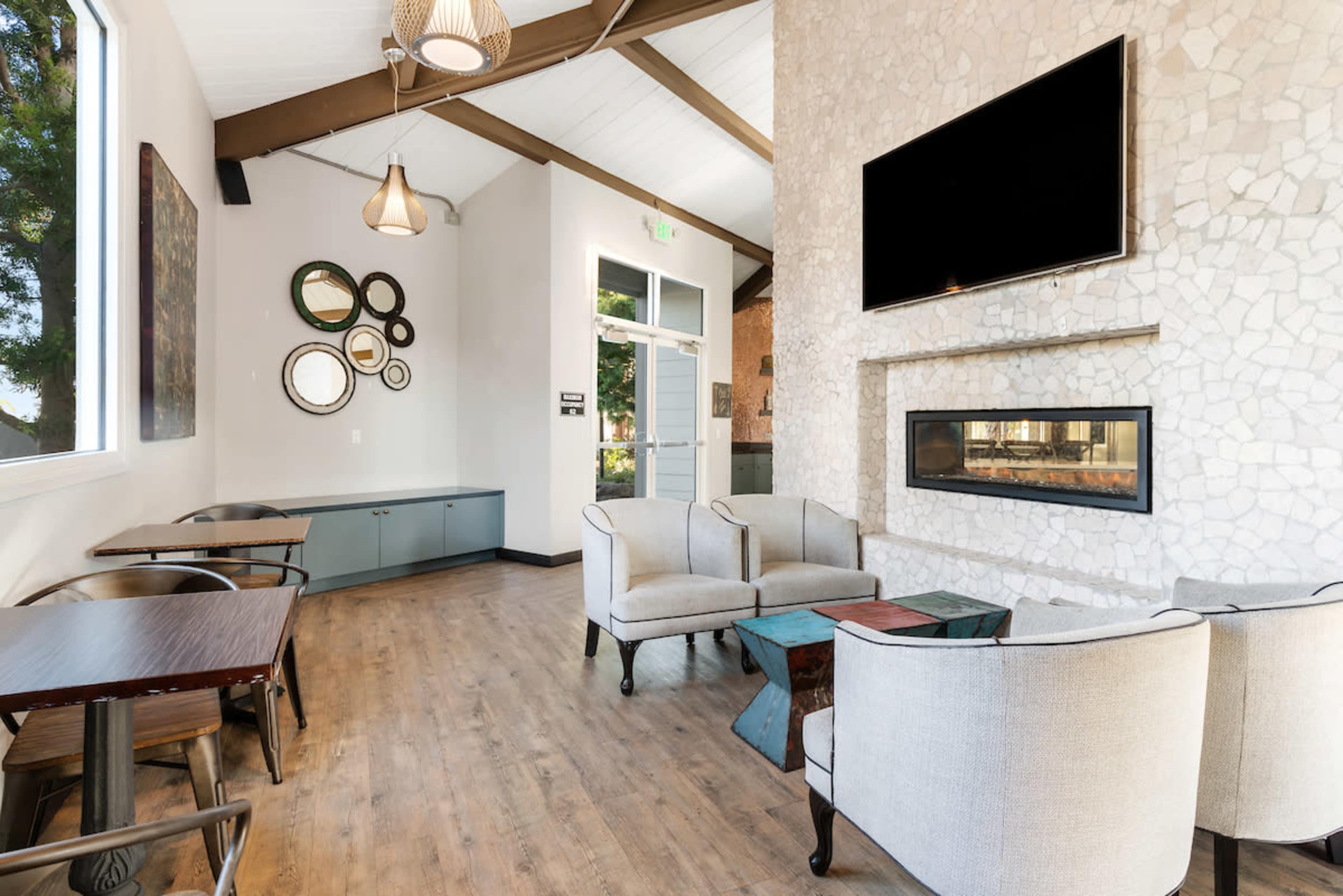 A modern lounge area with two armchairs, a coffee table, and a decorative wall featuring mirrors and a flat-screen TV above a stone fireplace.
