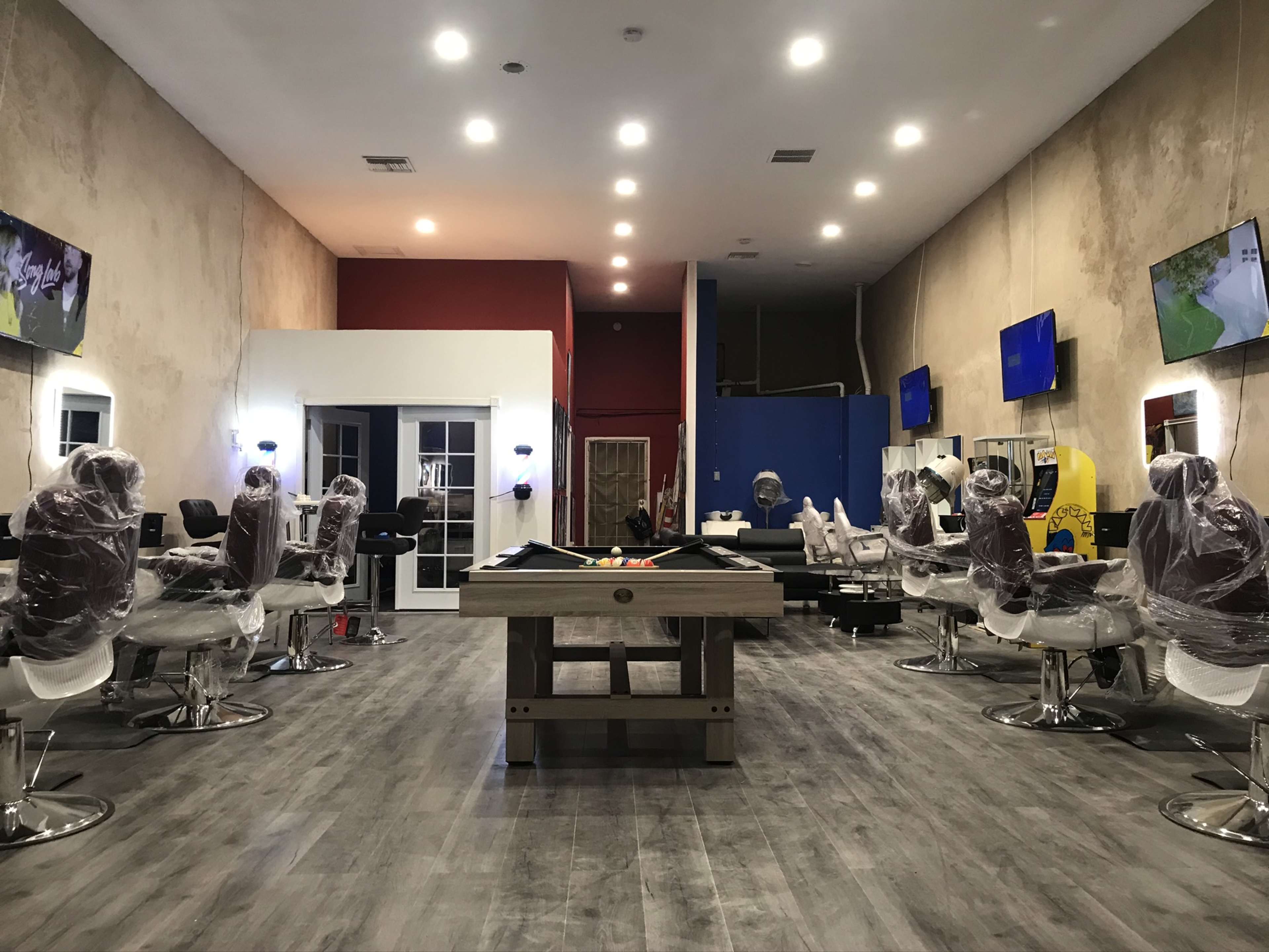 An empty hair salon with several styling stations, each covered with plastic, and two large televisions mounted on the walls.