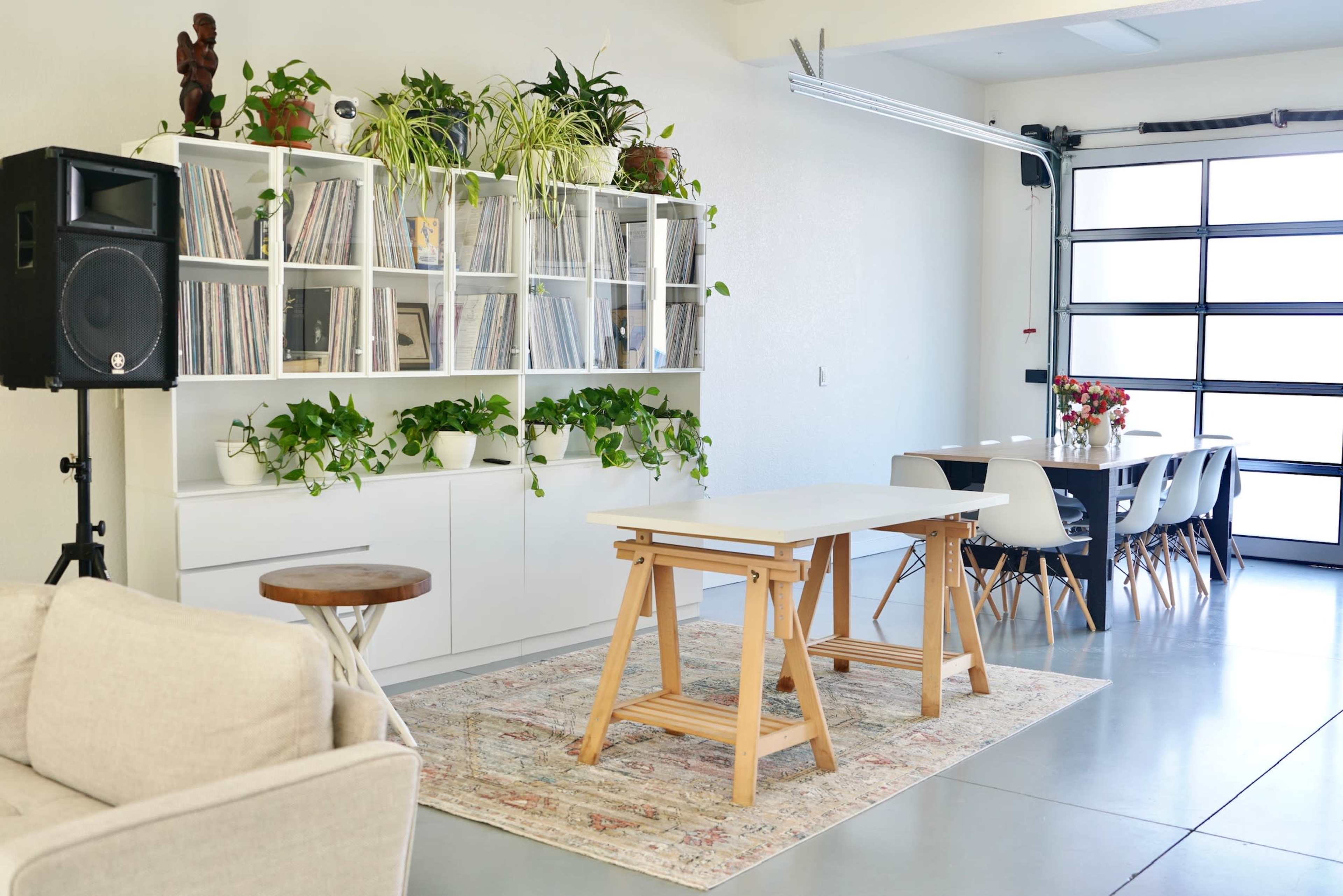 A modern, open space features a shelving unit filled with vinyl records, a large dining table, and a seating area with a light-colored sofa.