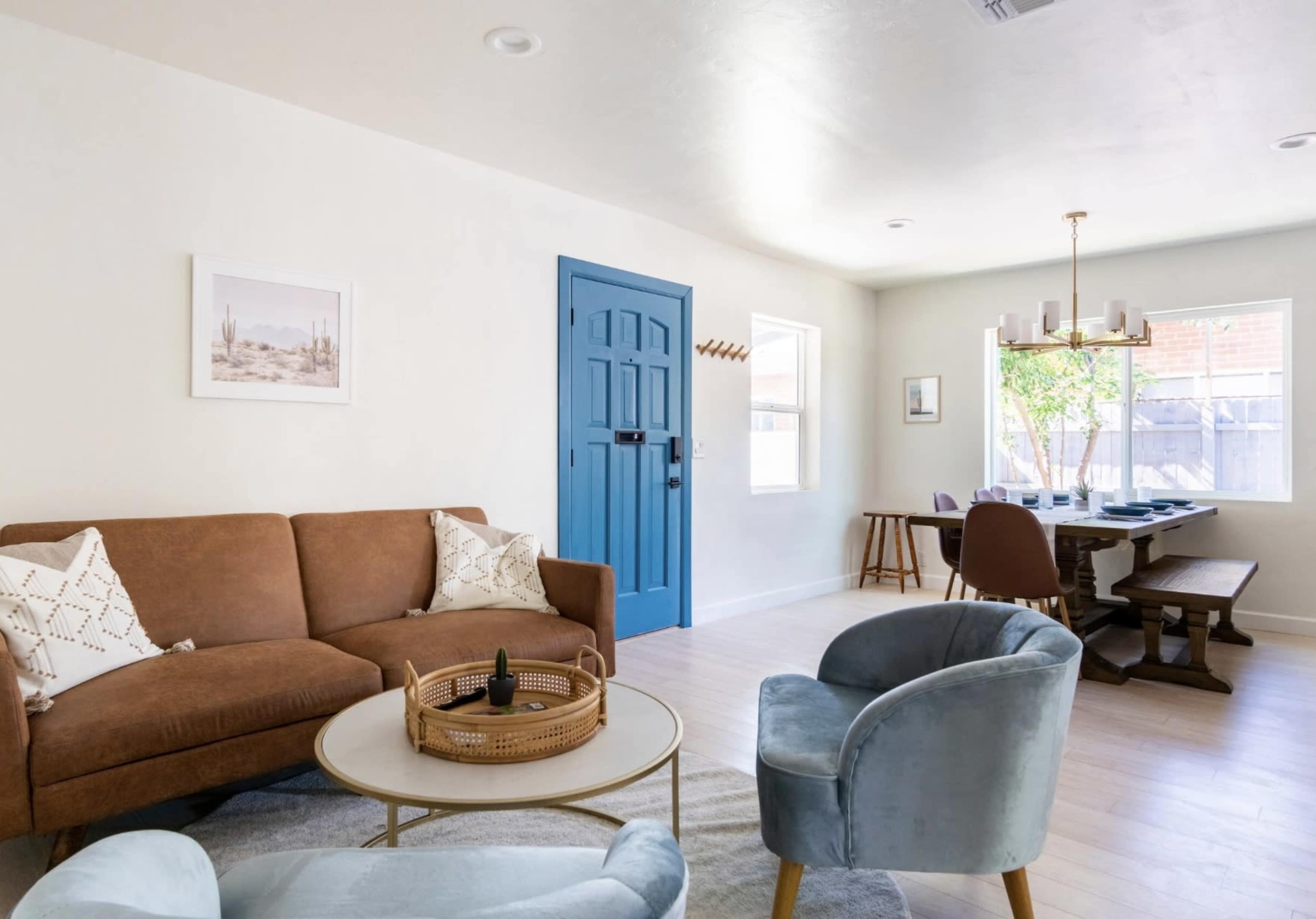 A living room features a brown couch, a blue door, and a dining table set against white walls.