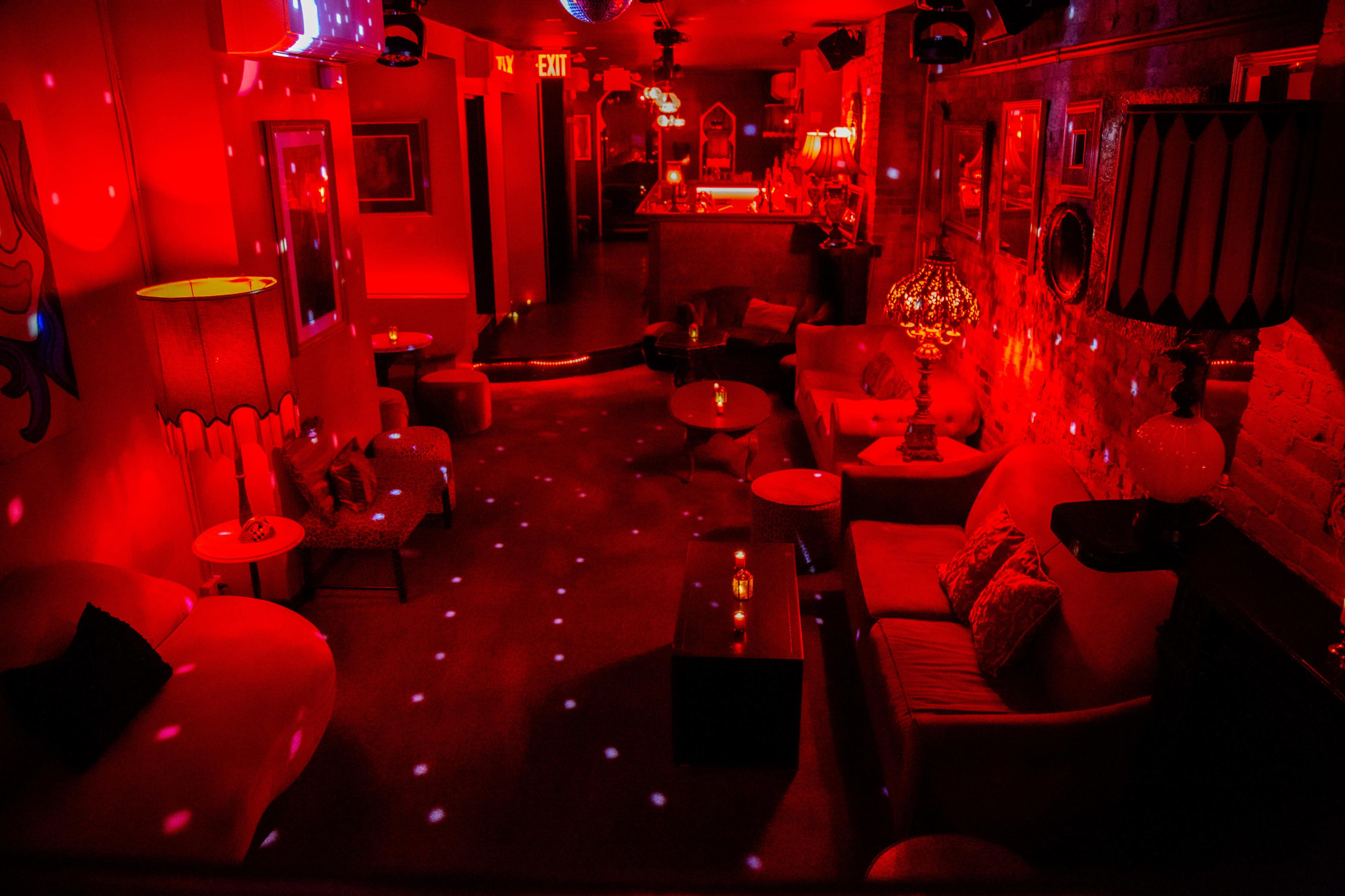 The image shows a dimly lit lounge decorated with red lighting, vintage furniture, and disco ball effects on the walls and floor.