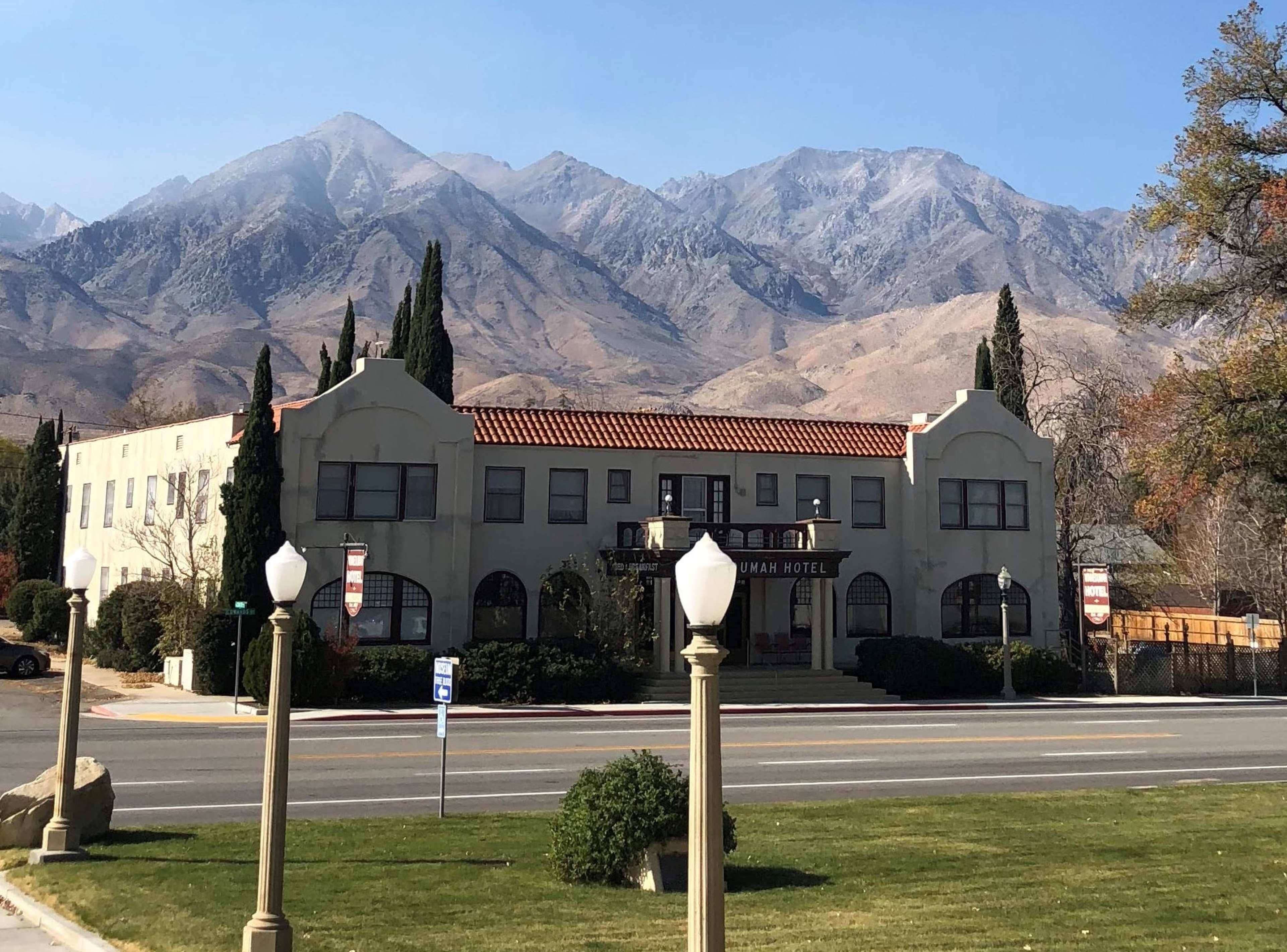 The image shows the front facade of the Manzanita Hotel, with mountains rising in the background under a clear sky.